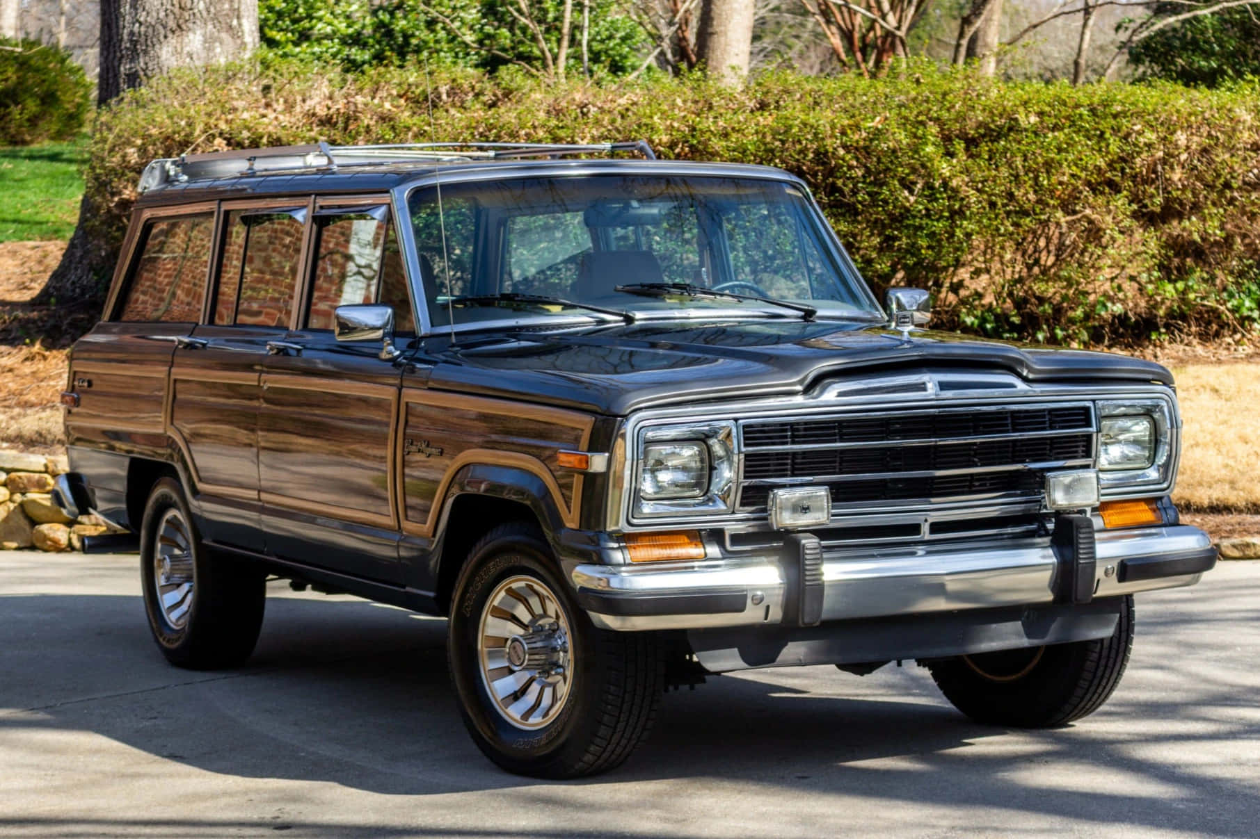Jeep Wagoneer 桌布 壁紙 — 一輛經典黑色Jeep Cherokee旅行車停在車道上，背景有樹木和灌木。