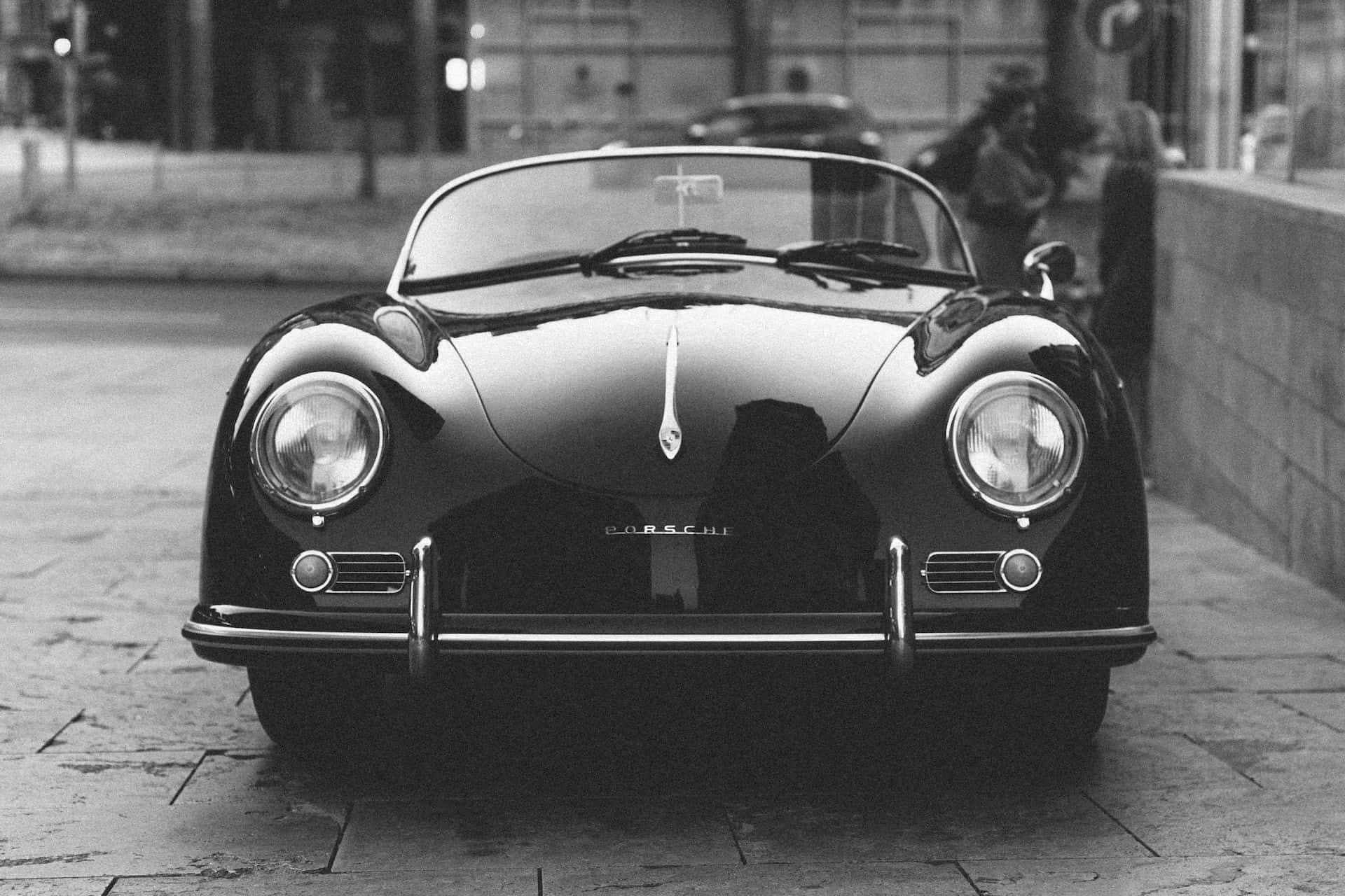 Black And White Car 桌布 壁紙 — 一輛經典黑色保時捷356敞篷車停泊在濕漉漉的鵝卵石街道上，以單色呈現，帶有倒影和柔和背景模糊效果。