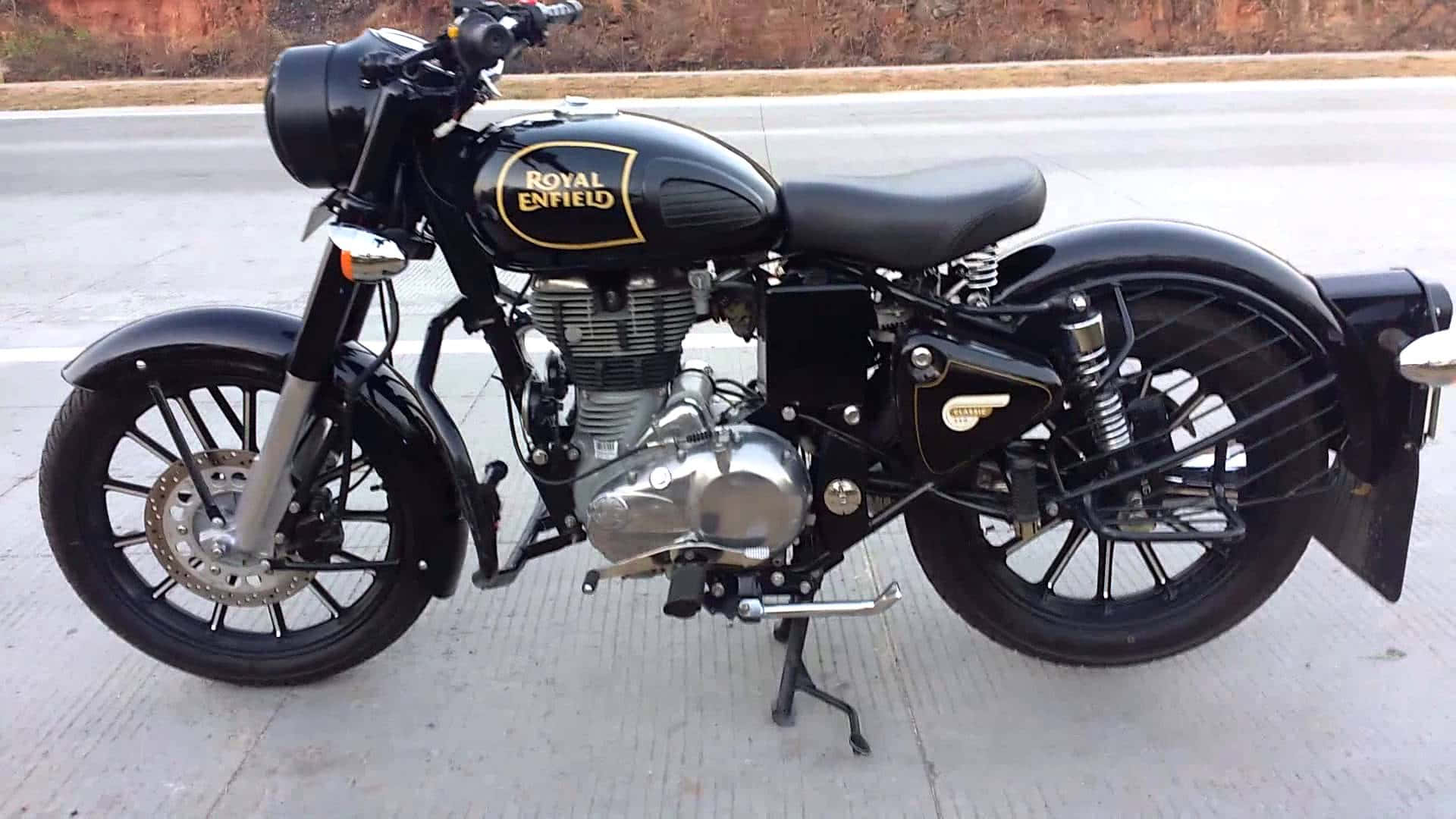 機車 桌布 壁紙 — 一輛經典黑色皇家恩菲爾德機車，帶有鍍鉻裝飾，在明亮的日光下立於混凝土表面上。