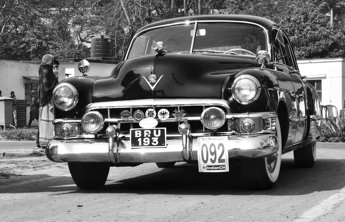 Black And White Vintage Car 桌布 壁紙 — 一輛經典黑色美國汽車，帶有鍍鉻細節和復古車牌，停在附近有人的街道上。