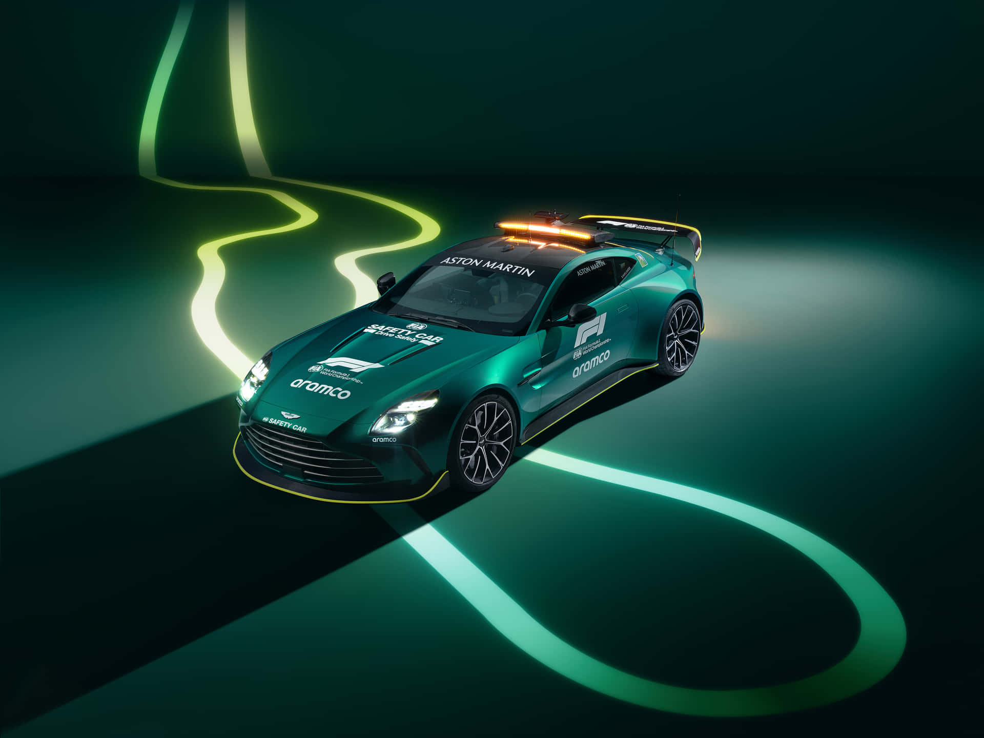 ASTON MARTIN SAFTEY CAR 壁紙 — 一輛綠色 Aston Martin F1 安全車，在黑暗的攝影棚地板上帶有發光的霓虹賽道線條。