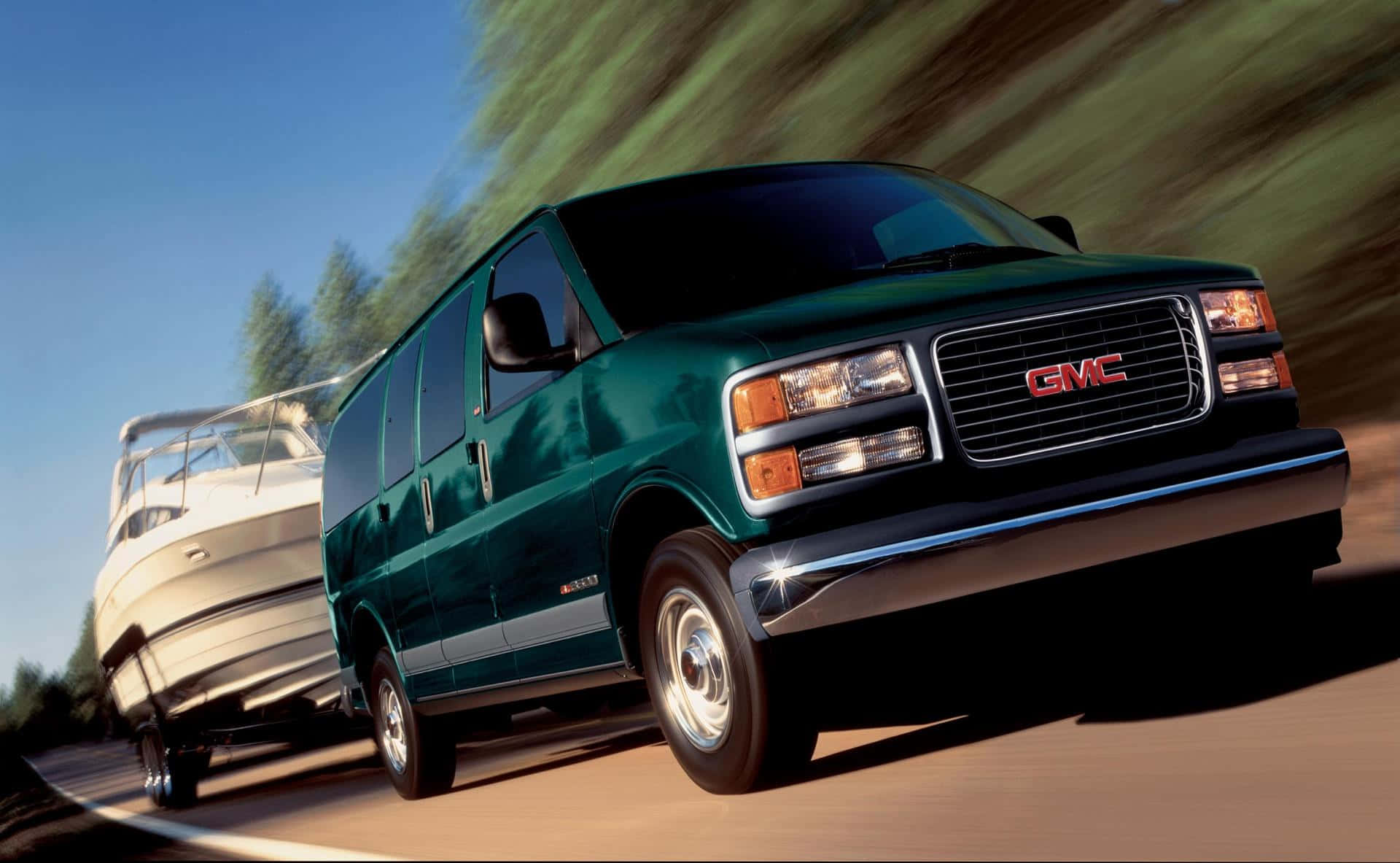 Gmc Savana 桌布 壁紙 — 一輛綠色GMC廂型車在道路上疾駛，拖著一艘白色船隻，背景是模糊的森林。