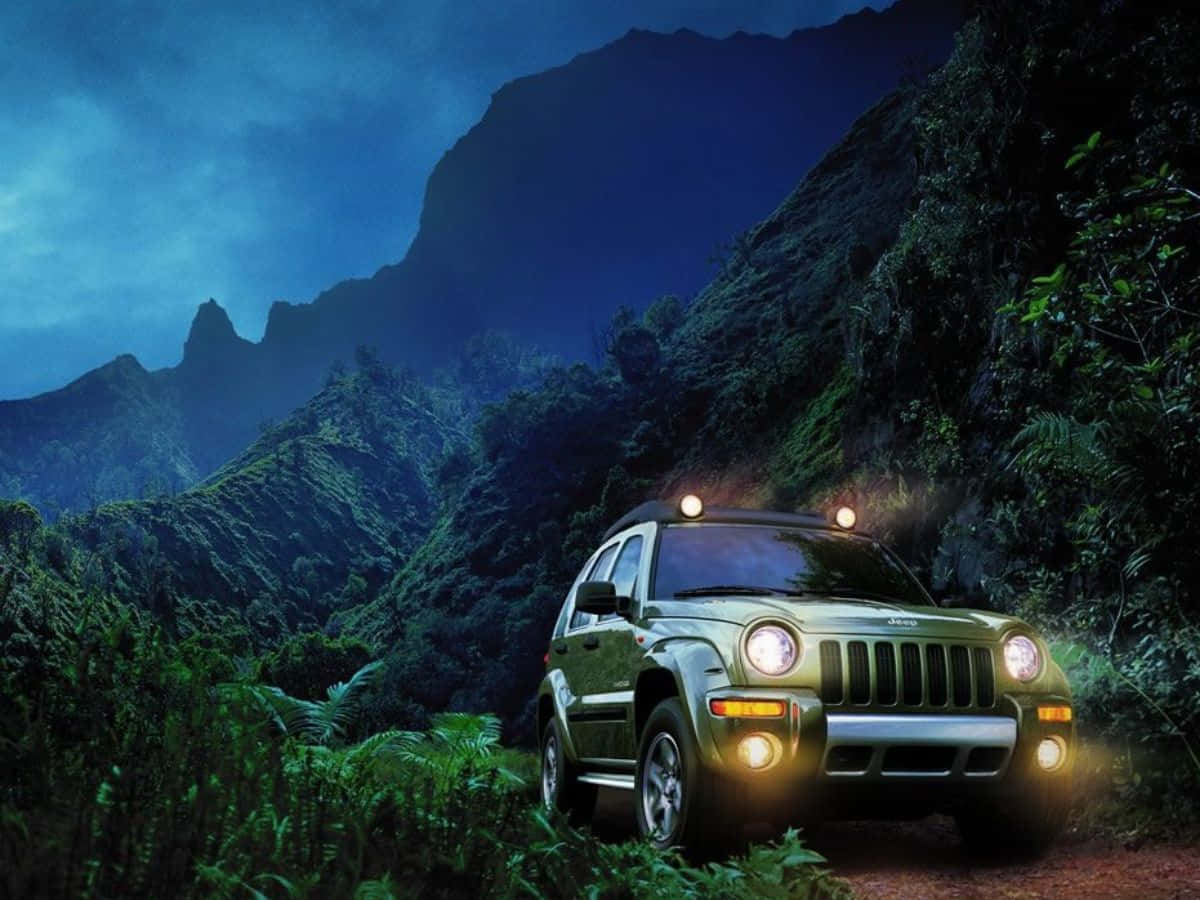 Jeep Liberty 桌布 壁紙 — 一輛綠色Jeep Wrangler亮著車頭燈，在暮色中穿過茂密叢林，背景是高聳的山脈。