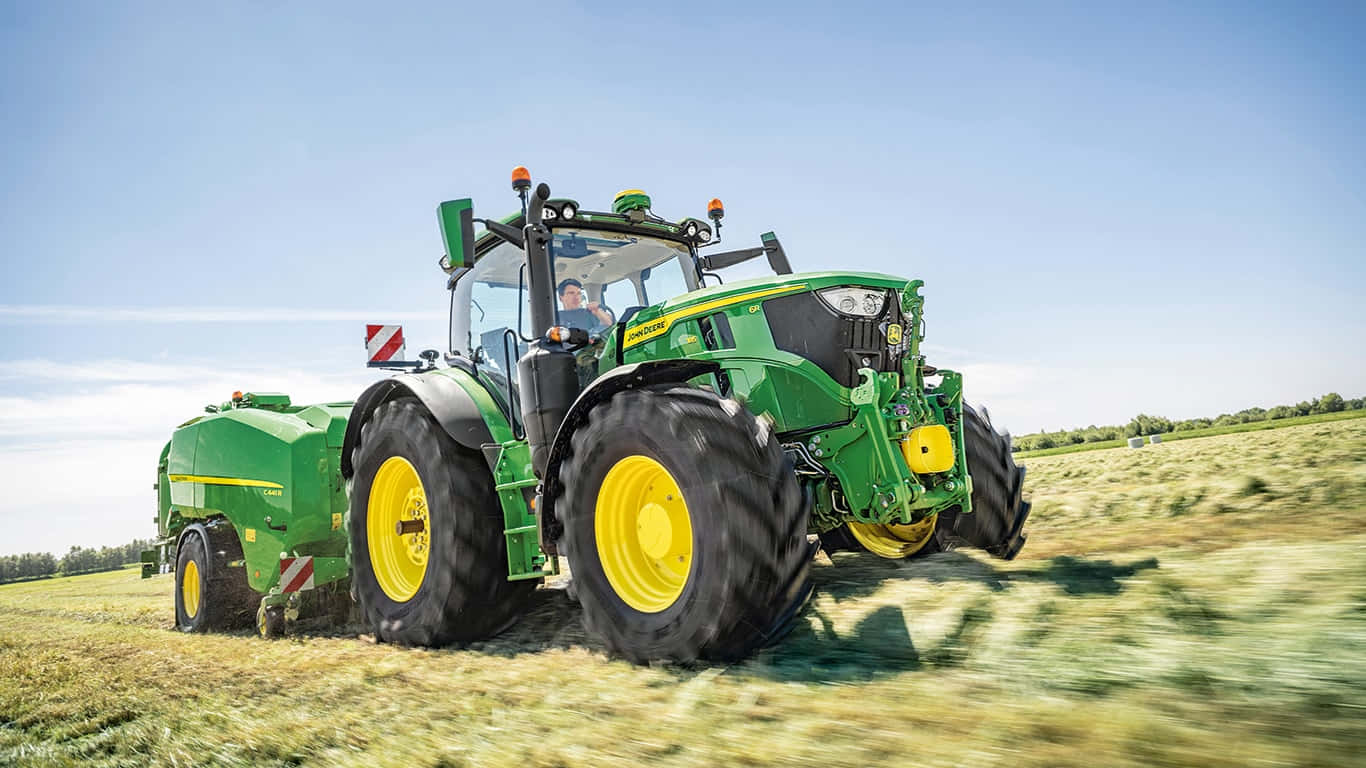John Deere 桌布 壁紙 — 一輛綠色John Deere拖拉機，黃色車輪，在晴朗藍天下飛馳過陽光照耀的田野。