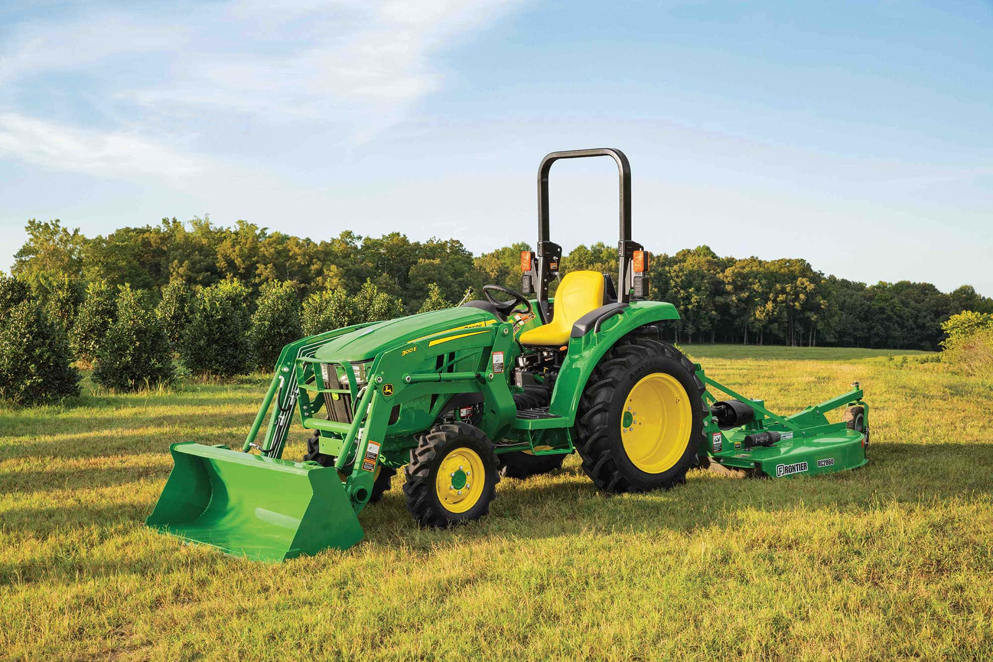 Tractor 桌布 壁紙 — 一輛綠色John Deere拖拉機，帶有黃色車輪和附件，站在陽光明媚的草地上，周圍樹木環繞，天空清澈湛藍。