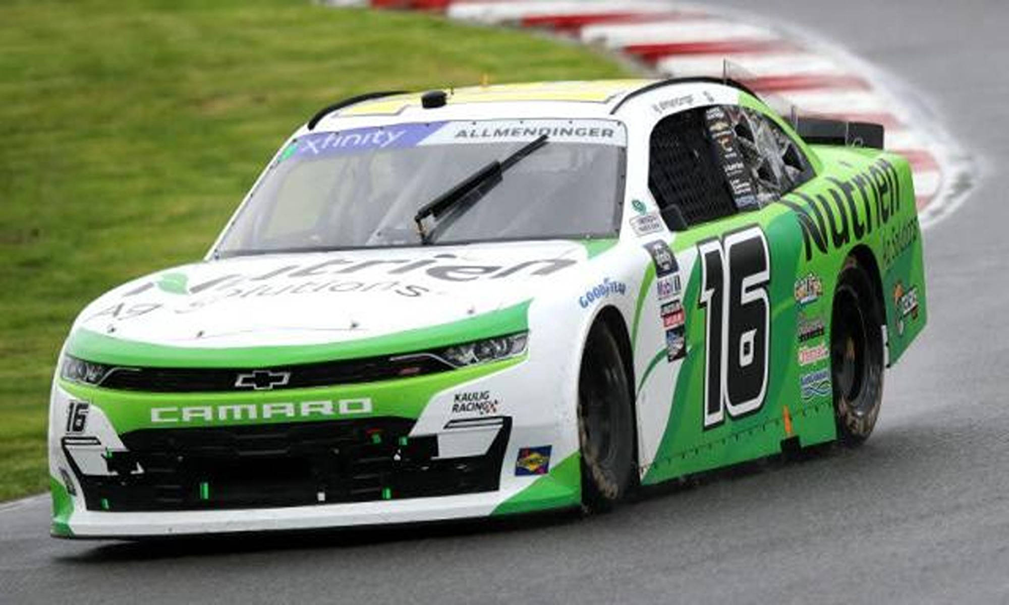 Racing 桌布 壁紙 — 一輛綠色和白色的 #16 雪佛蘭 Camaro NASCAR 賽車在潮濕的賽道彎道上高速行駛，背景有草地和紅白相間的路緣石。