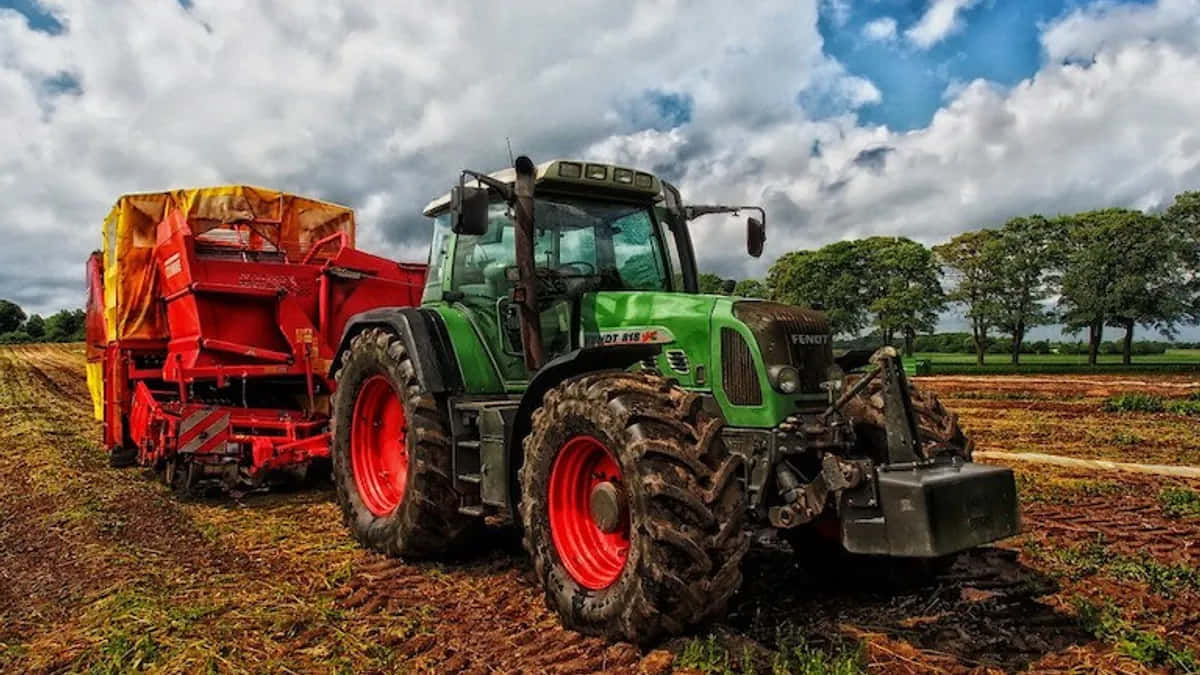 Farming 桌布 壁紙 — 一輛綠色和紅色的拖拉機，輪胎沾滿泥濘，在陰天下拉著一輛紅色乾草車穿過收割後的田野。