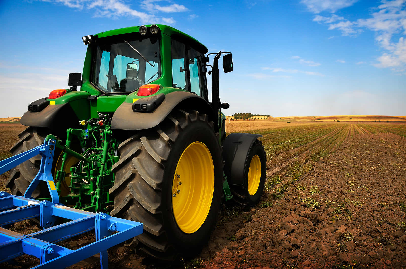 Tractor 桌布 壁紙 — 一輛綠色和黃色的約翰迪爾拖拉機拖著藍色的犁，在明亮的藍天和散落的雲朵下，穿過新翻的棕色土壤。