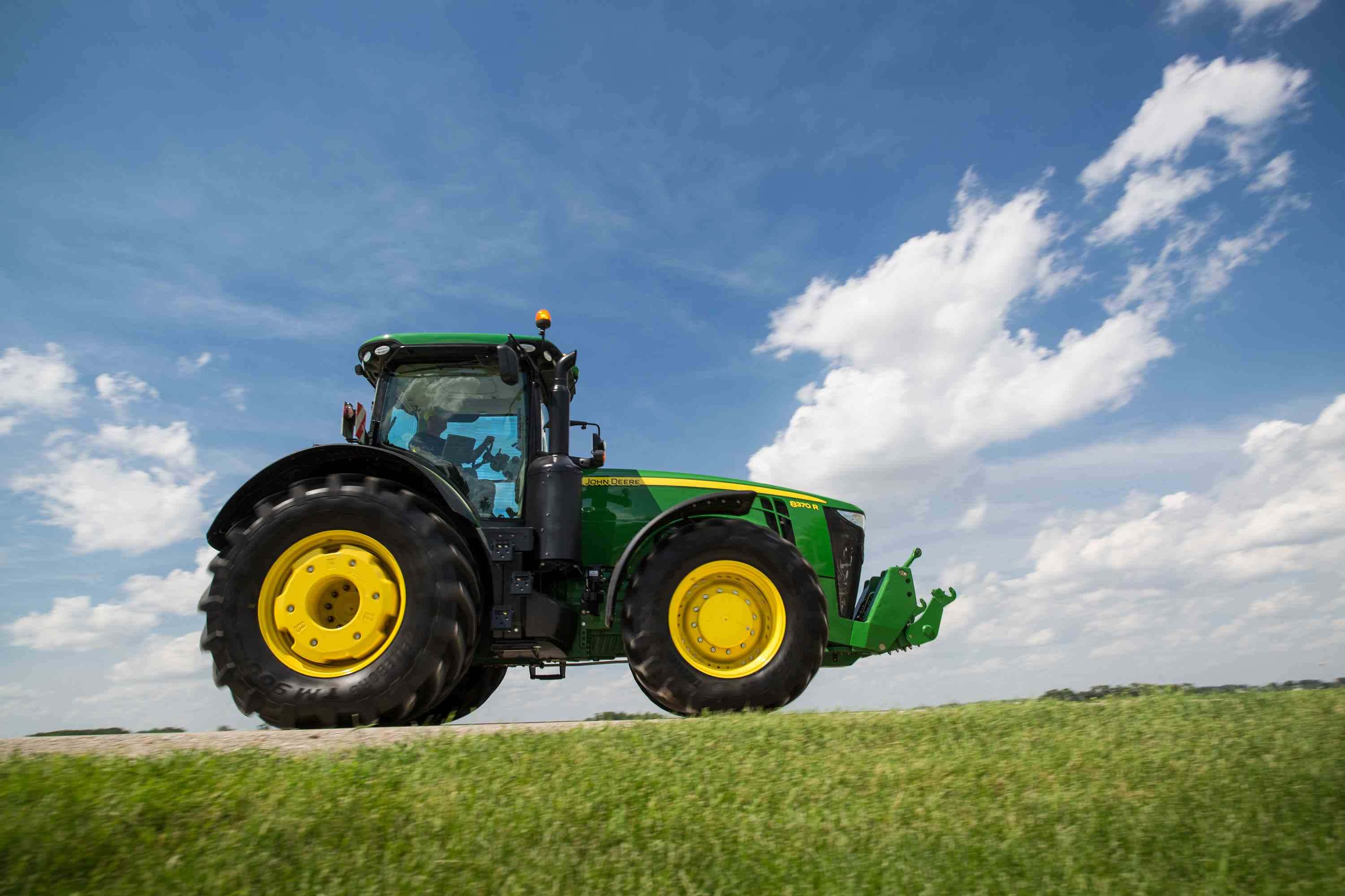 Tractor 桌布 壁紙 — 一輛綠色和黃色的約翰迪爾拖拉機站在長滿草的田野上，天空湛藍，白雲蓬鬆。