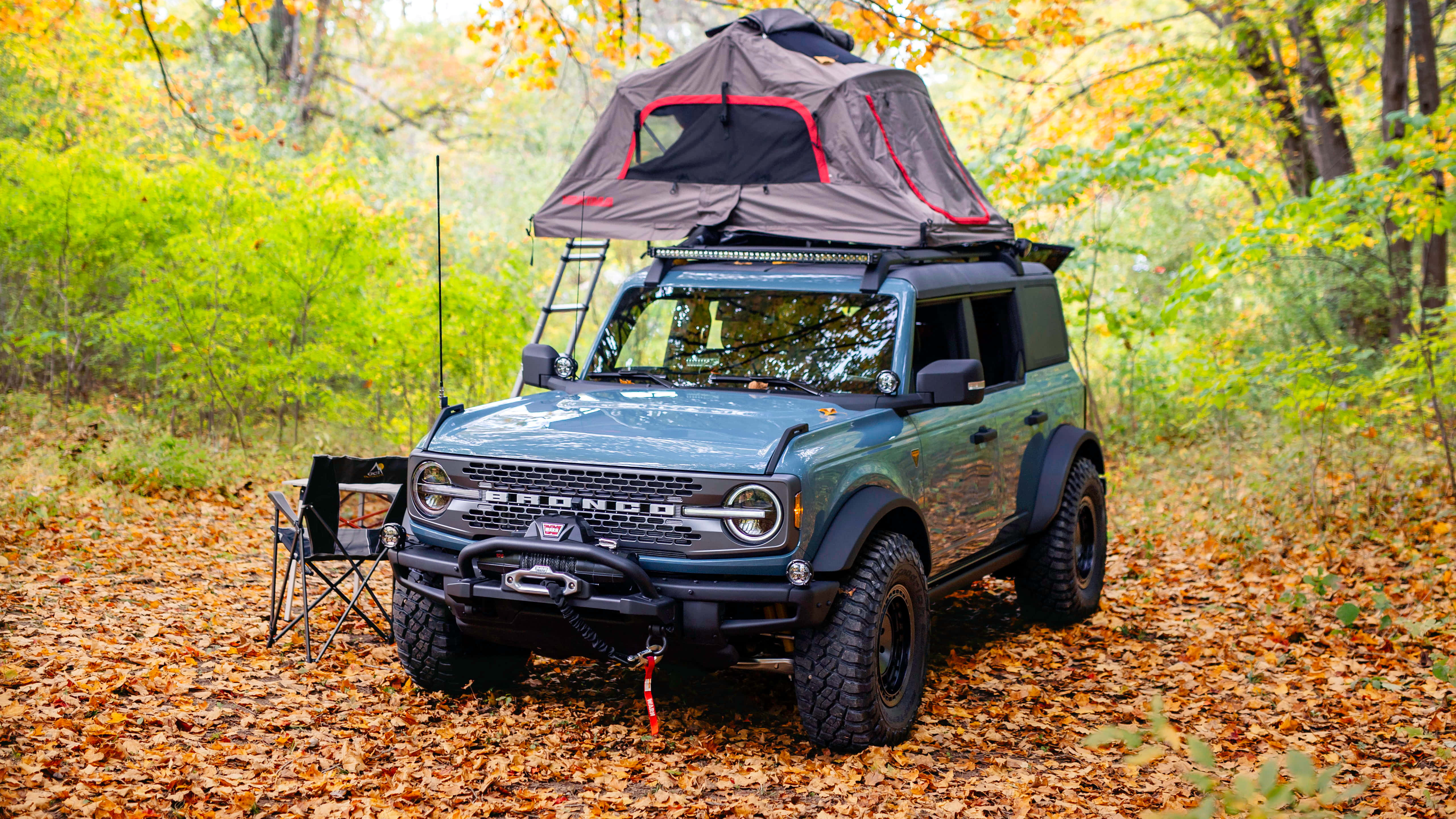 Ford Bronco 桌布 壁紙 — 一輛綠色福特Bronco配備車頂帳篷，停泊在鋪滿金色秋葉的森林中。