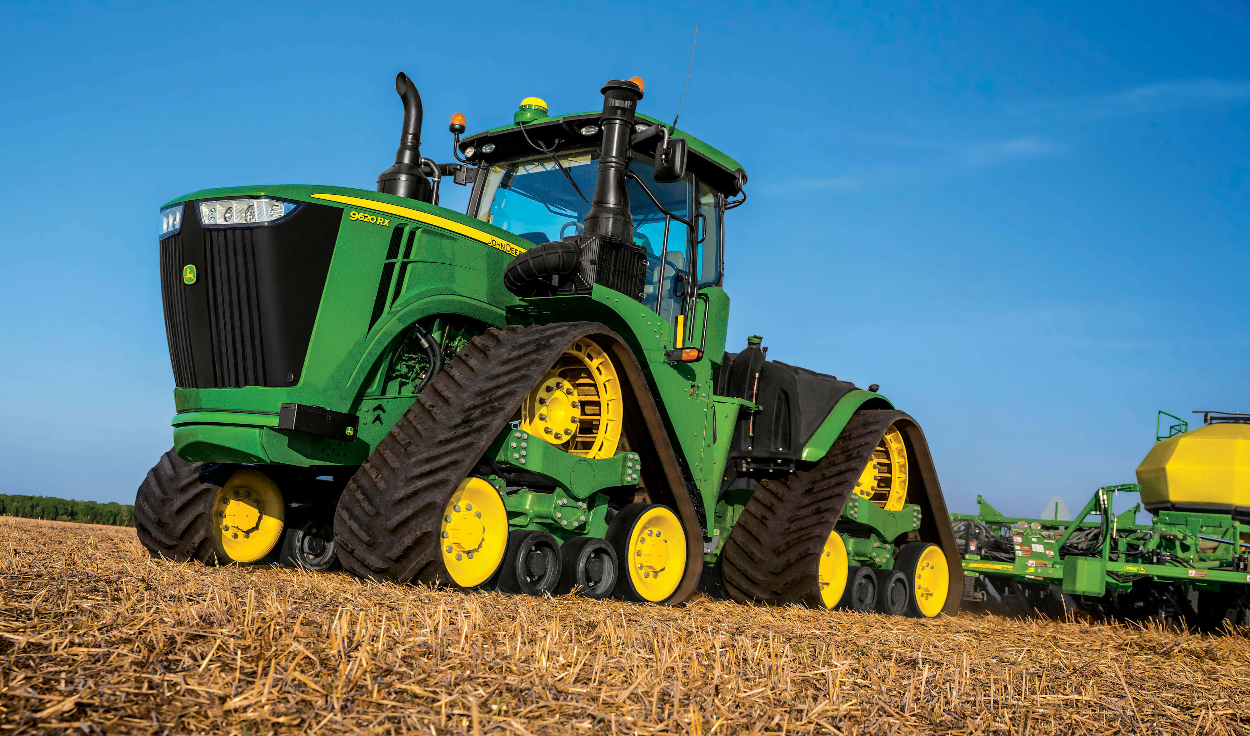 Tractor 桌布 壁紙 — 一輛綠色約翰迪爾履帶拖拉機帶有黃色輪子，站在晴朗藍天下已收割的田地中。