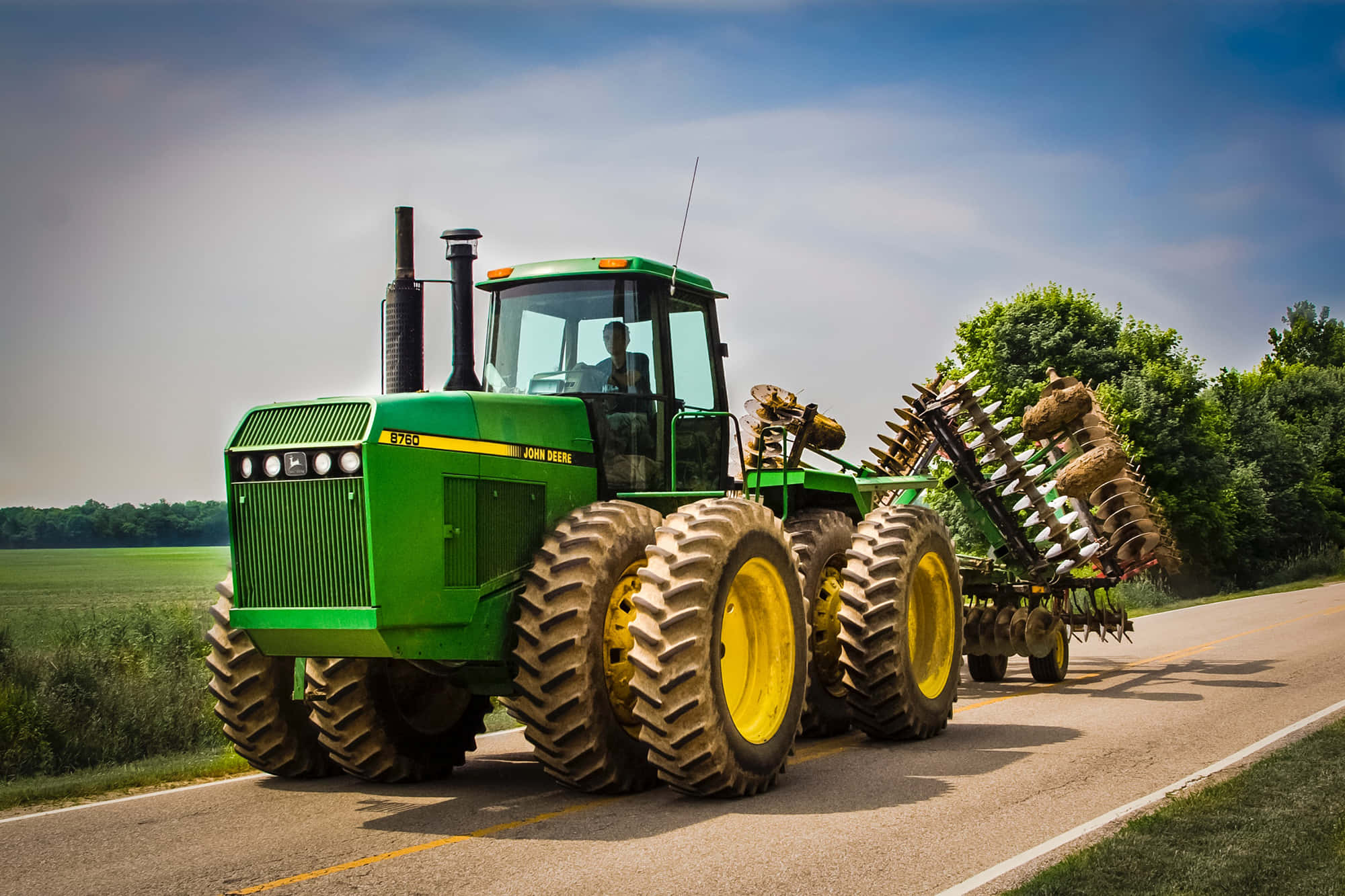 Tractor 桌布 壁紙 — 一輛綠色約翰迪爾拖拉機，黃色車輪，在明亮的藍天下沿著鄉村道路拉犁。