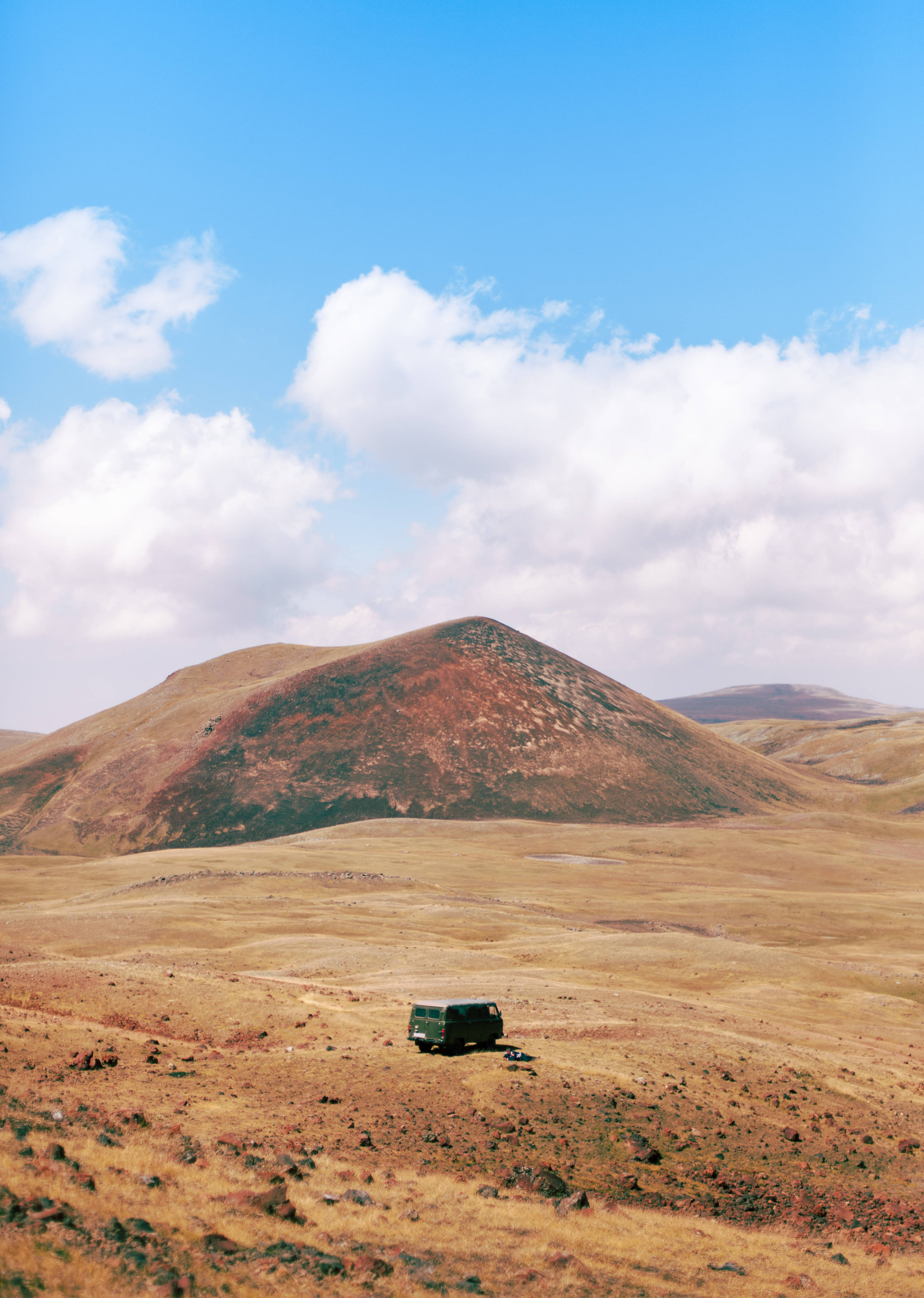 Armenia 桌布 壁紙 — 一輛綠色貨車獨自停放在廣闊的金色草地上，頭頂是明亮的藍天和蓬鬆的白雲。