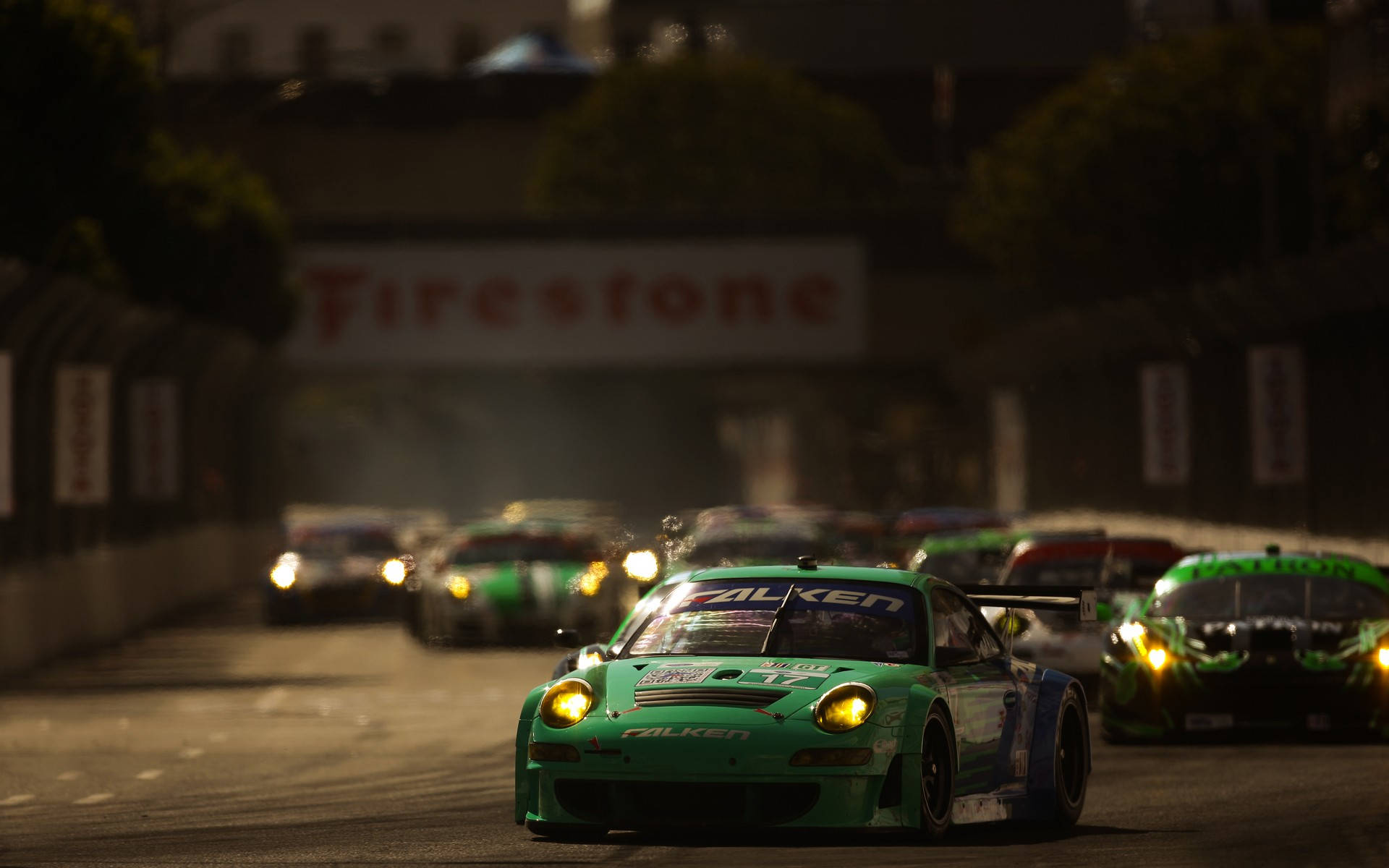 Auto Racing 桌布 壁紙 — 一輛綠色賽車配備明亮車頭燈，在「Firestone」標誌下，帶領一群競爭對手穿過昏暗的夜間賽道。