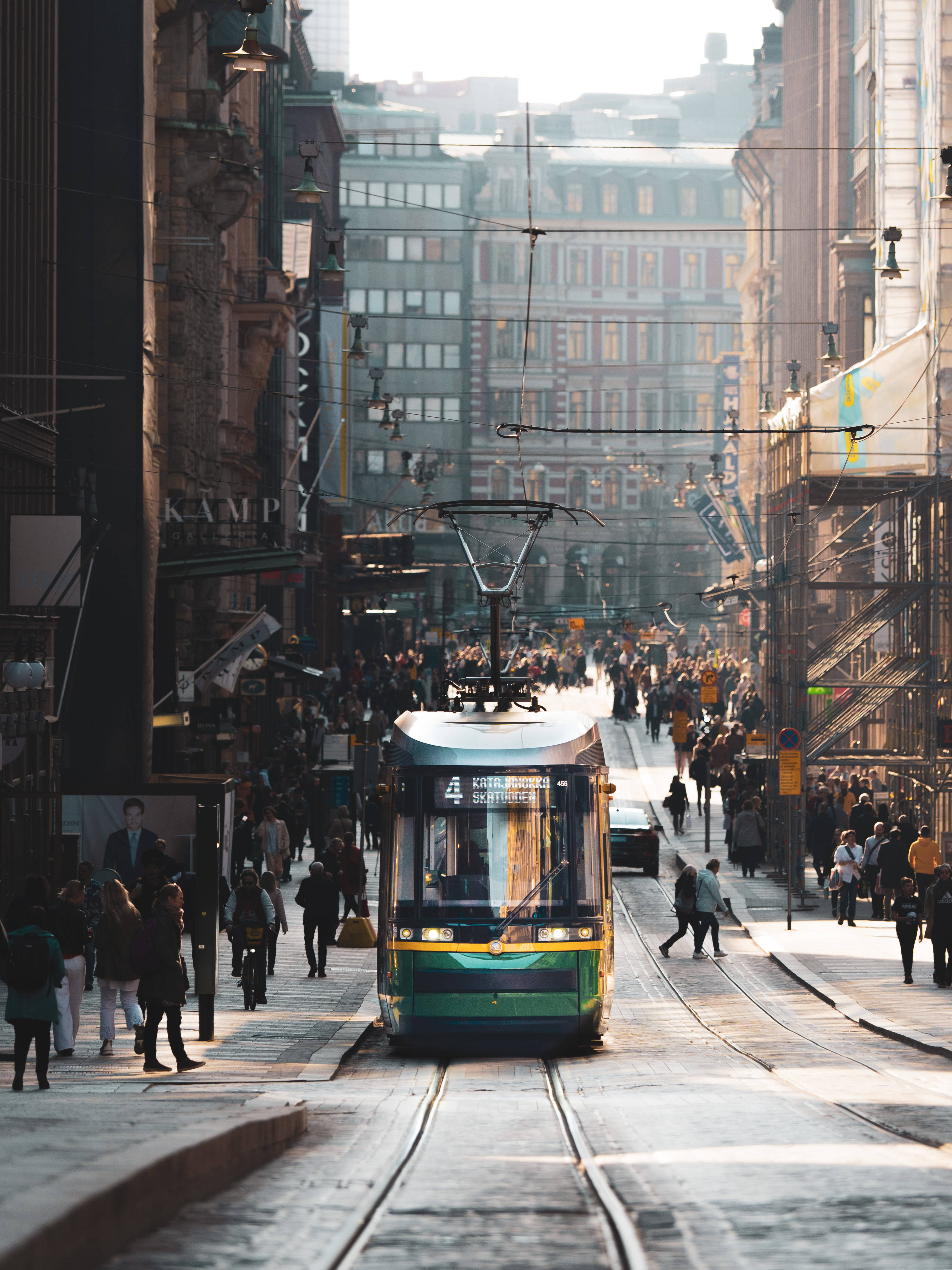Finland 桌布 壁紙 — 一輛綠色電車在繁華的歐洲城市街道上滑行，兩旁是歷史建築，行人沐浴在金色的夕陽中。