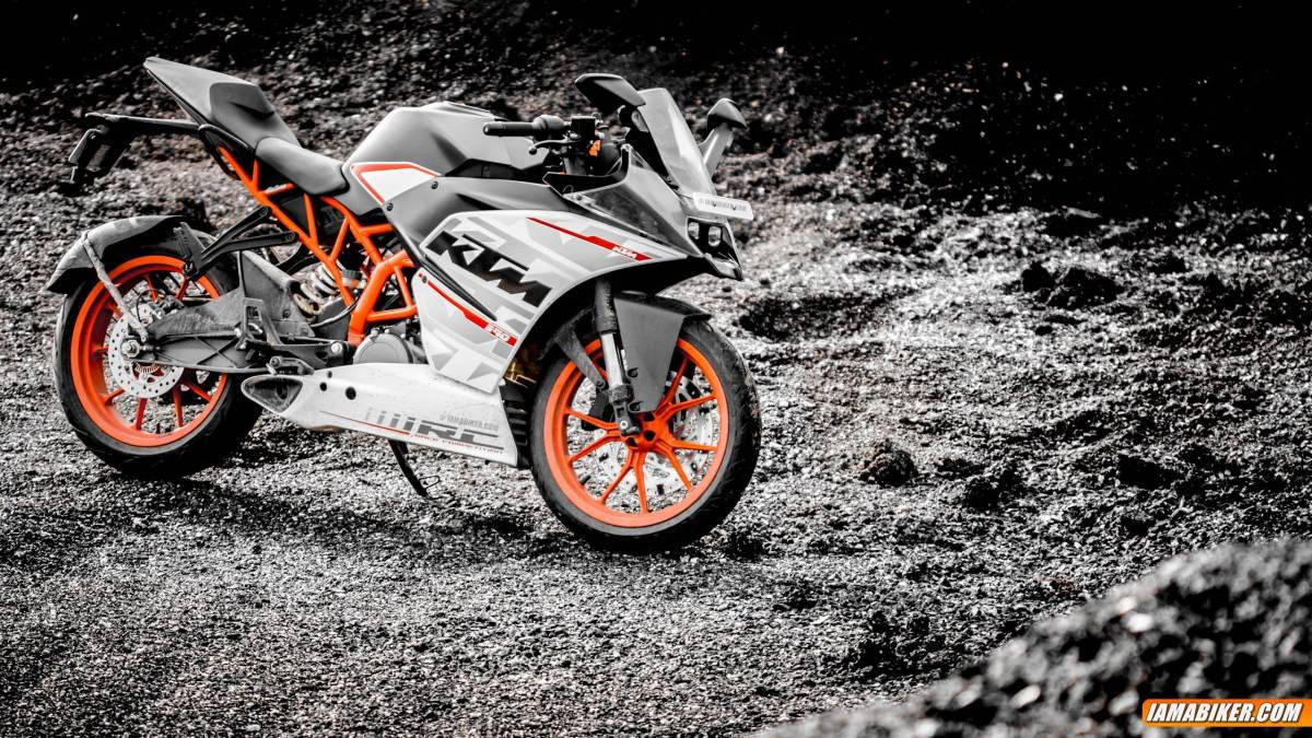 KTM 摩托車 桌布 壁紙 — 一輛線條流暢的KTM機車，帶有鮮豔的橙色點綴，在戲劇性的單色燈光下，停在粗糙的礫石表面上。