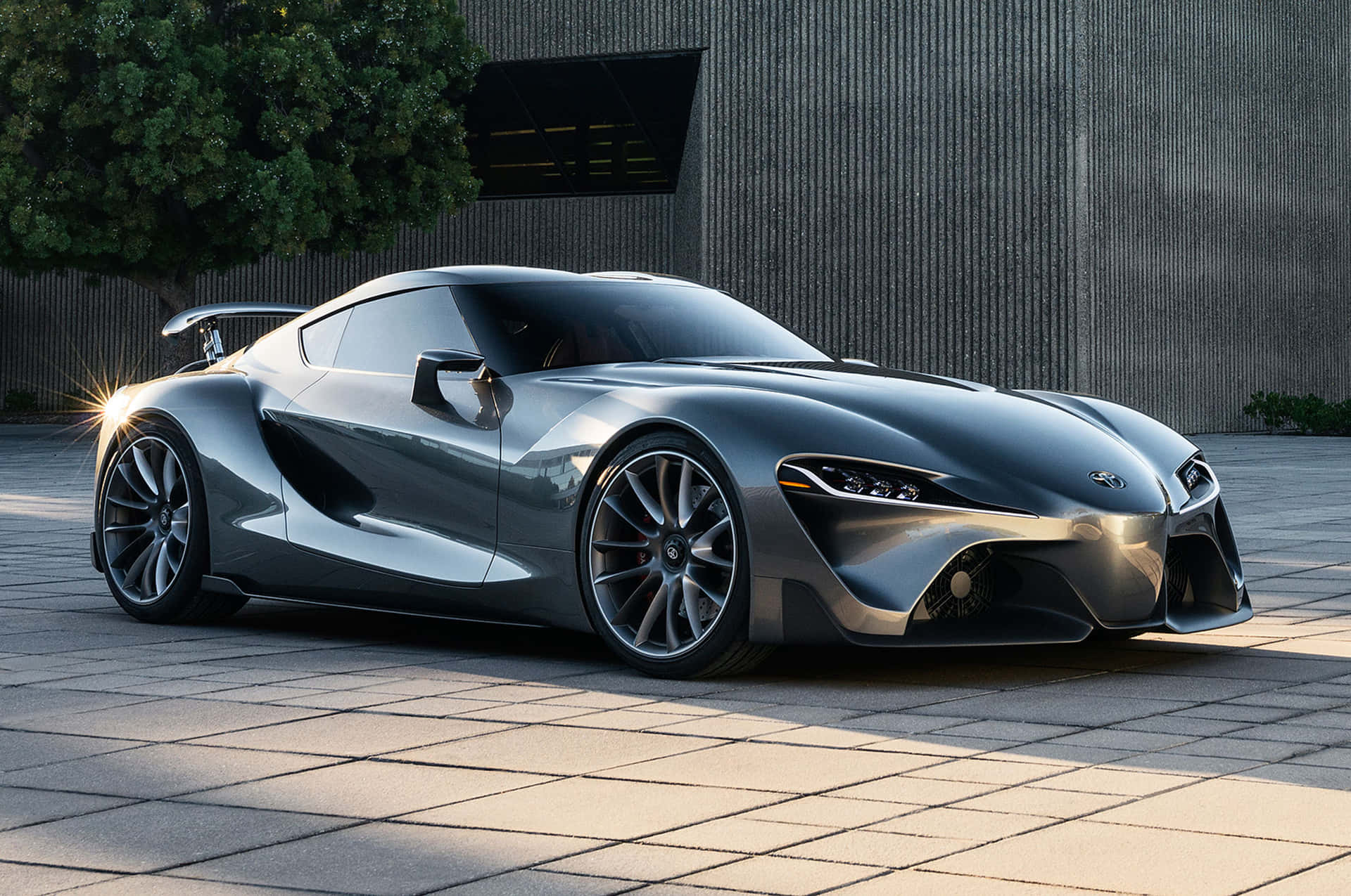 銀色未來感跑車停泊在現代建築附近的鋪砌廣場上。 — Toyota Supra Mk4 壁紙