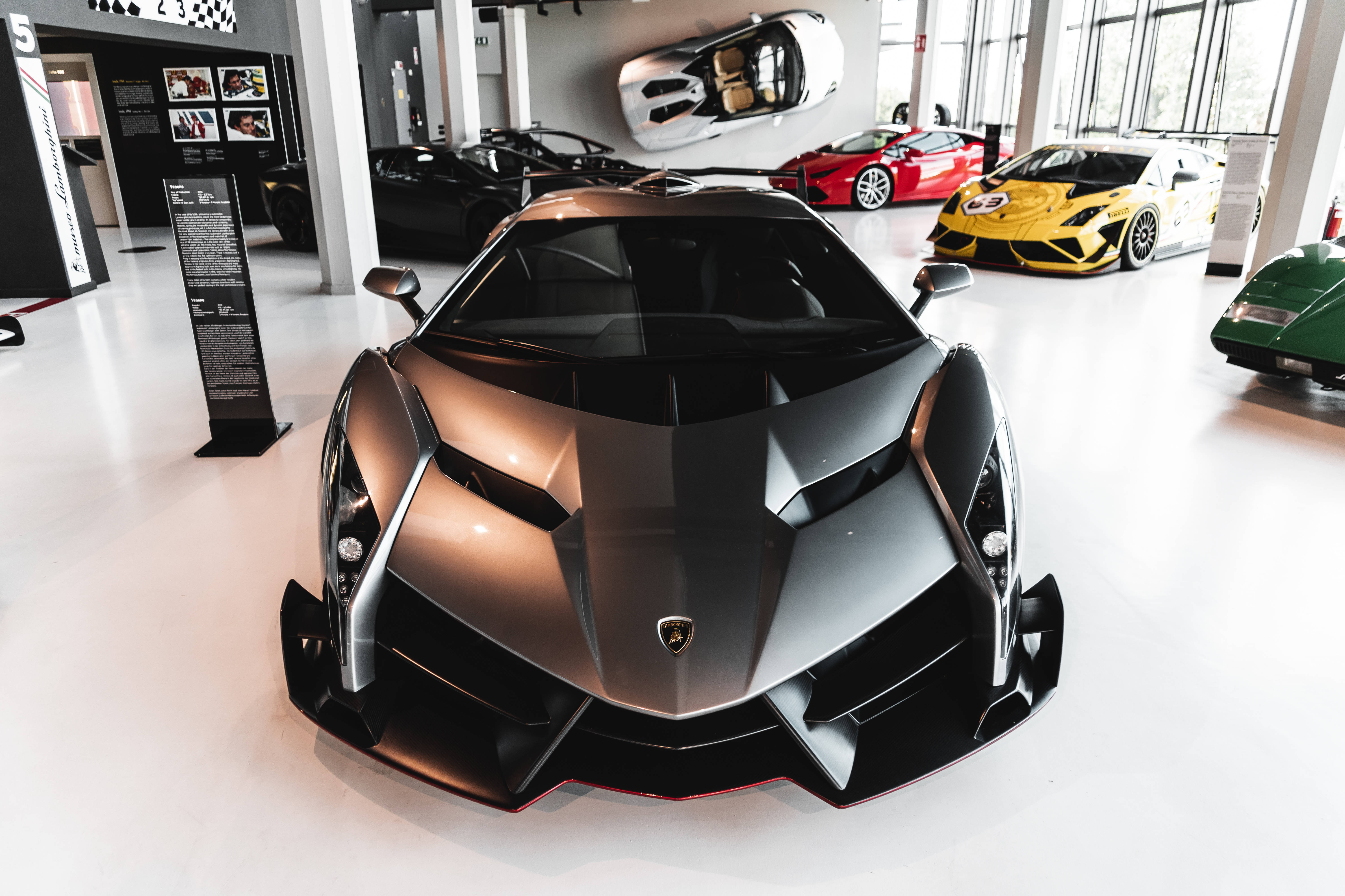 Luxury 桌布 壁紙 — 一輛線條流暢的黑色藍寶堅尼 Veneno，帶有銳利角度和紅色點綴，在明亮的現代汽車展示間中與其他豪華跑車一同佔據主導地位。