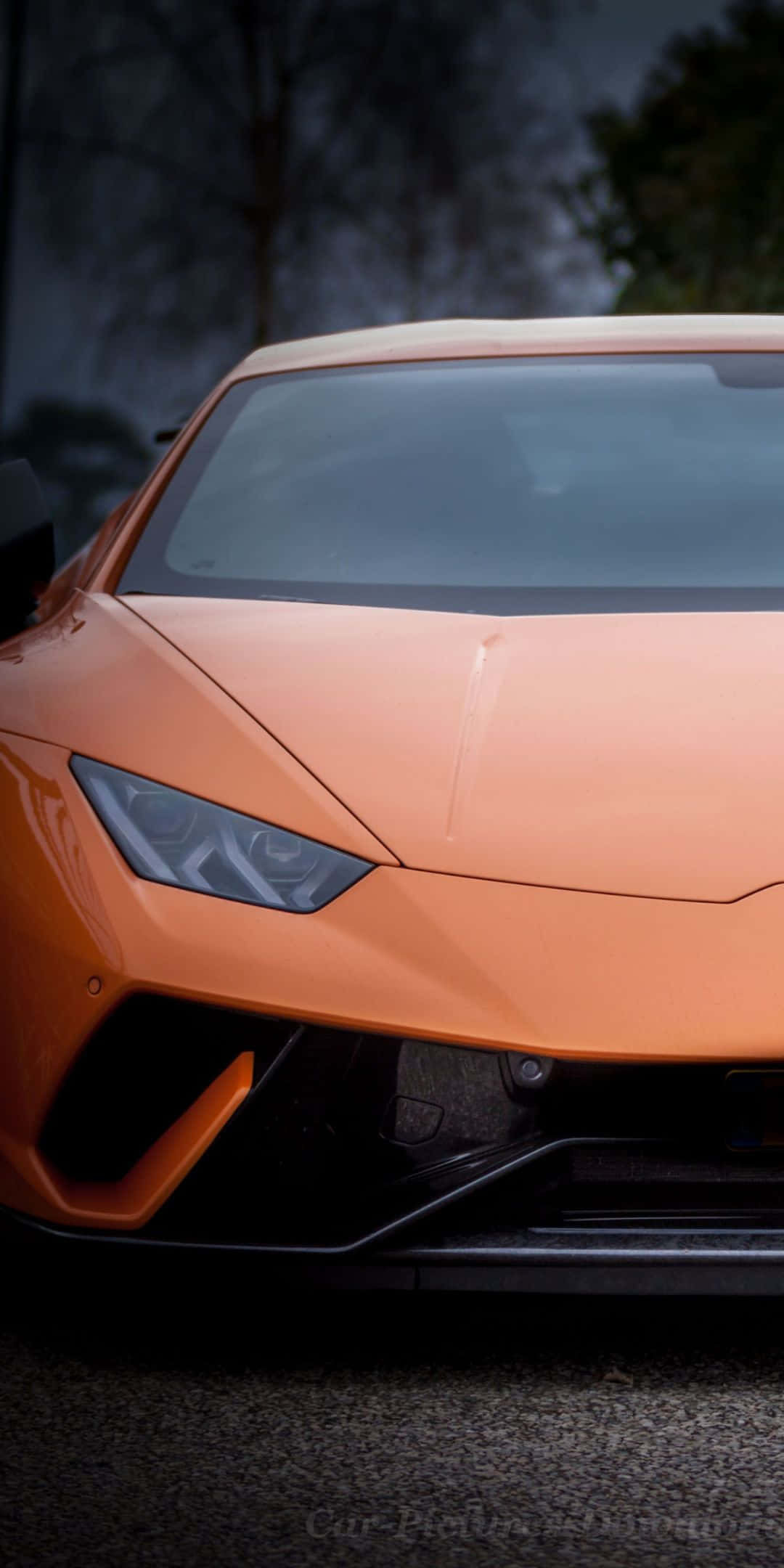 Pixel 3 Lamborghini 桌布 壁紙 — 一輛線條銳利、車頭燈發光的時尚橙色跑車的特寫，停泊在深色瀝青路面上。