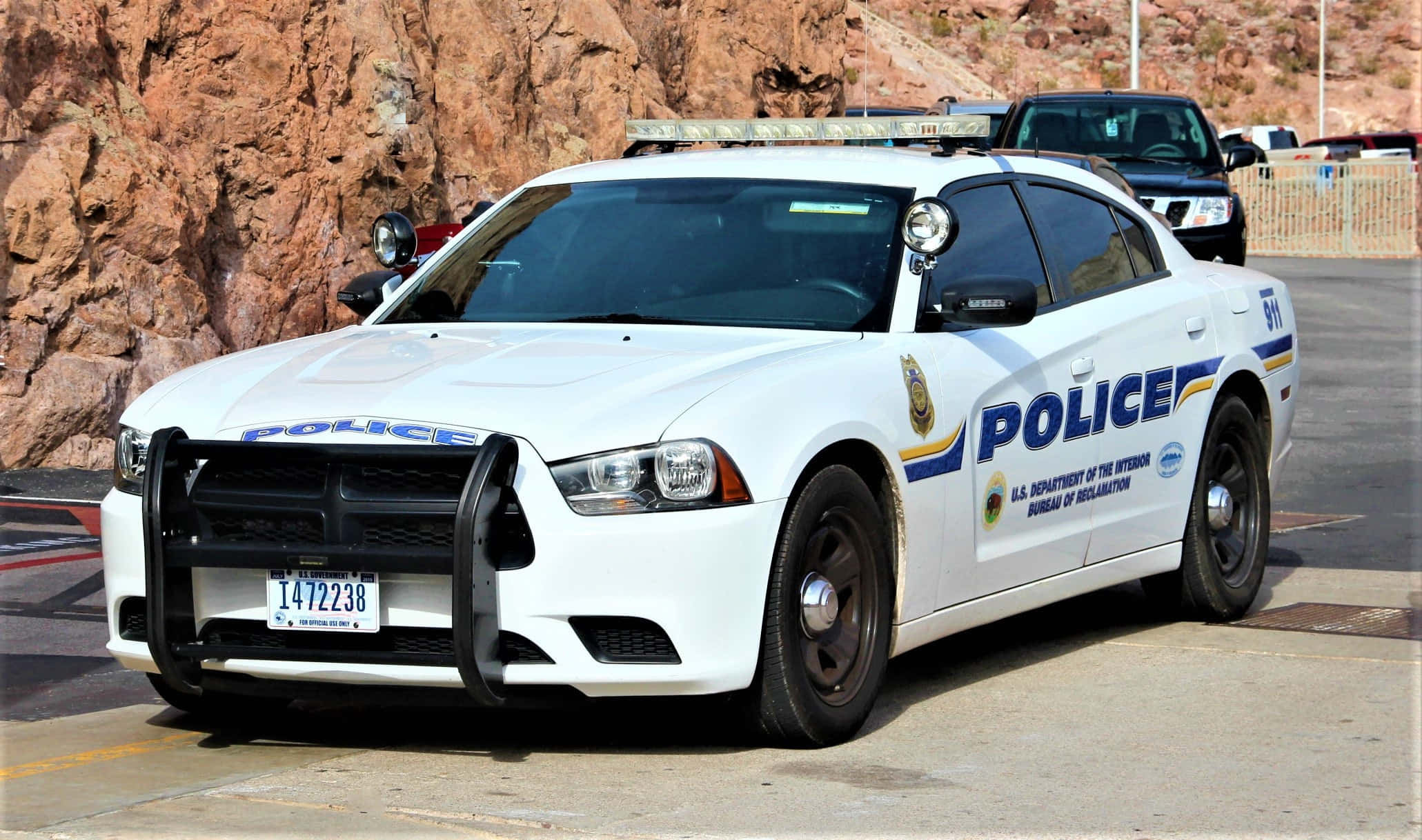 Police Car 桌布 壁紙 — 一輛美國墾務局的白色警車停在鋪砌的停車場上，旁邊是岩石峭壁，在明亮的日光下。