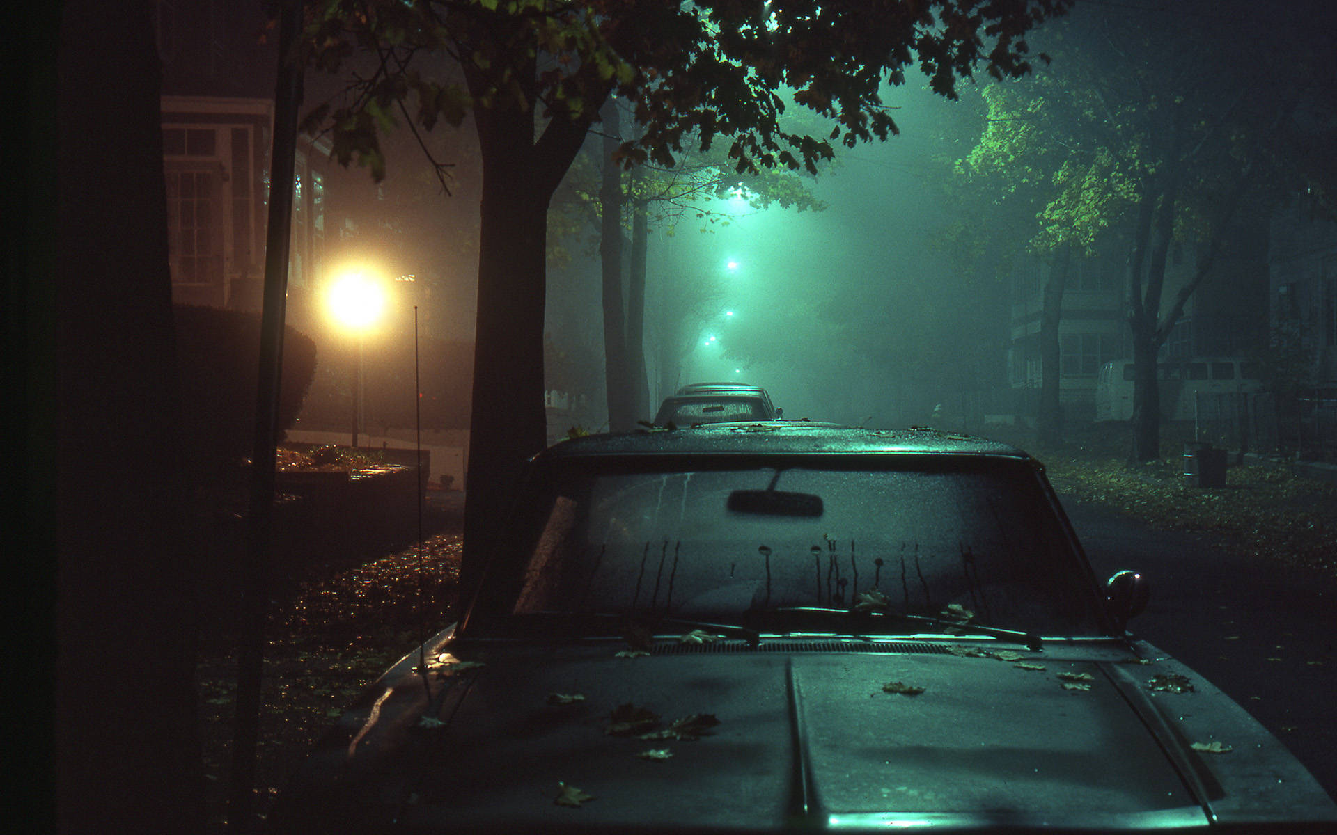 Night Aesthetic 桌布 壁紙 — 一輛老爺車在夜晚被遺棄在霧氣瀰漫的街道上，被詭異的綠色街燈和一盞溫暖的黃燈照亮。