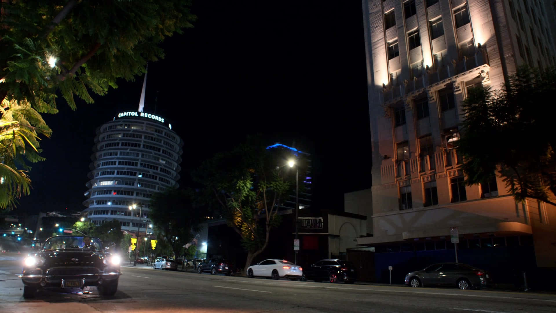 Road 桌布 壁紙 — 一輛老爺車在夜間駛過城市街道，經過燈火通明的 Capitol Records 大樓和經典建築。
