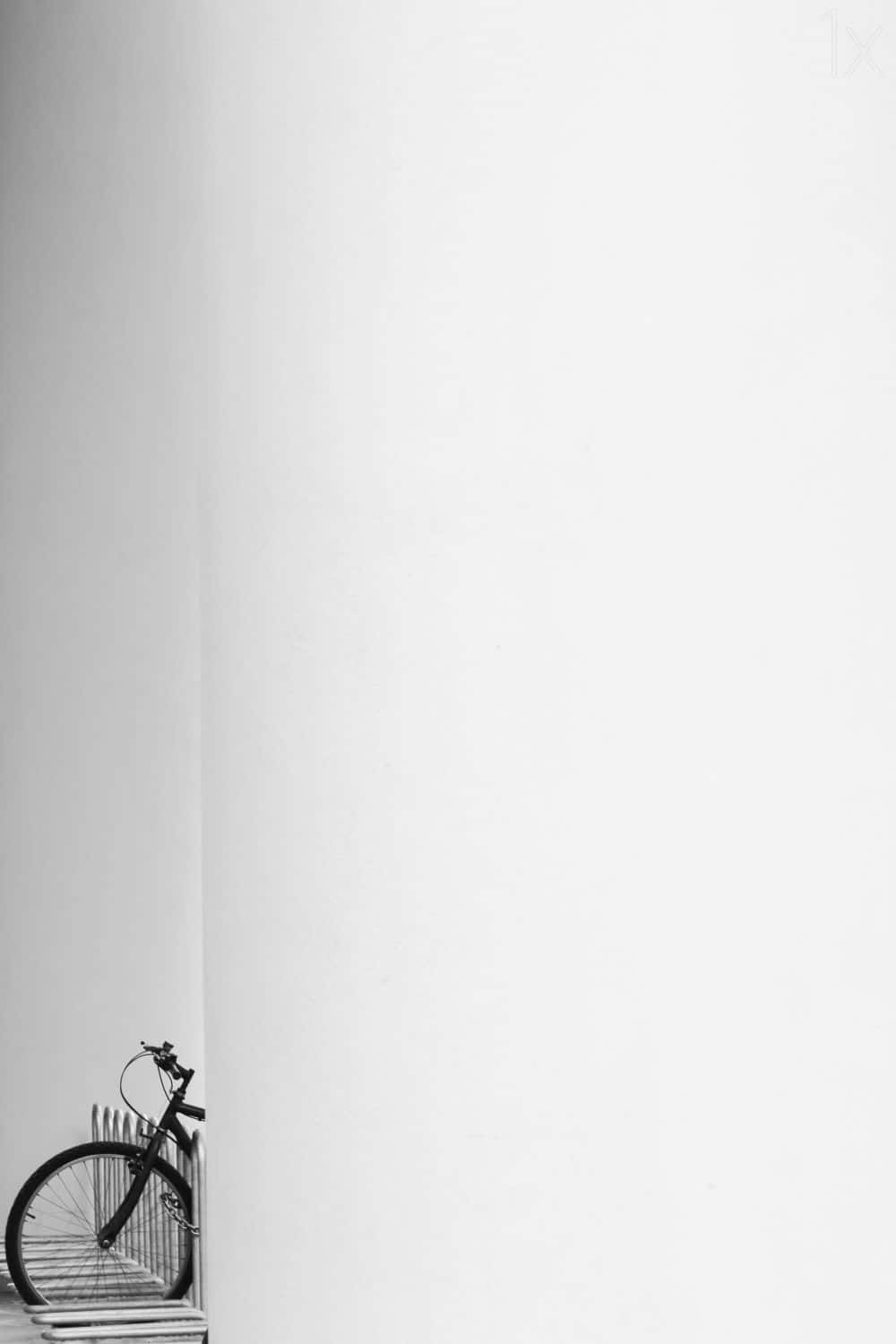 Minimalist Photography 桌布 壁紙 — 一輛腳踏車停放在都市環境中純白牆壁旁的極簡黑白照片。