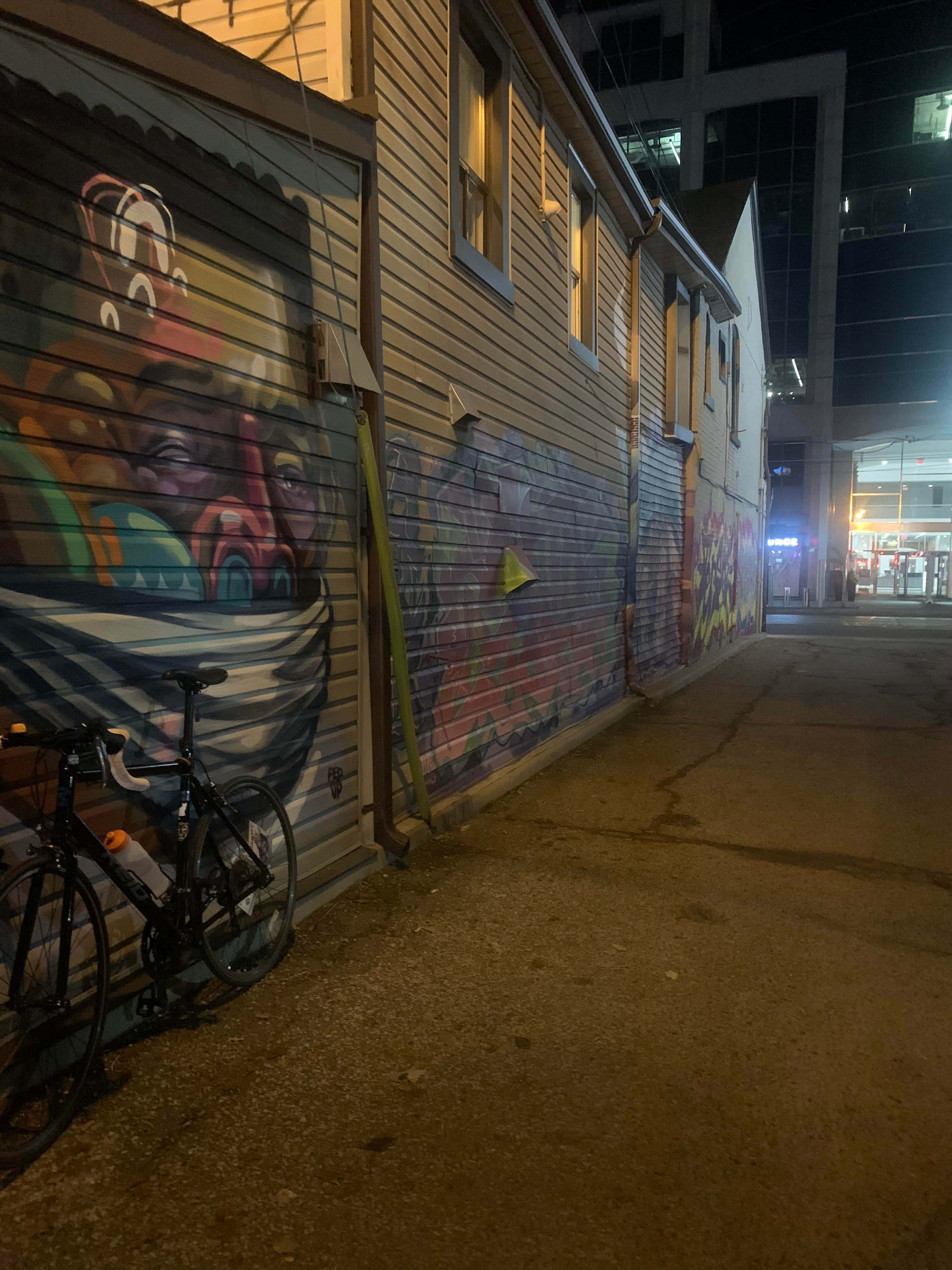 Ghetto Hood 桌布 壁紙 — 一輛腳踏車在夜晚的城市燈光下靠在一條充滿活力的塗鴉小巷牆上。