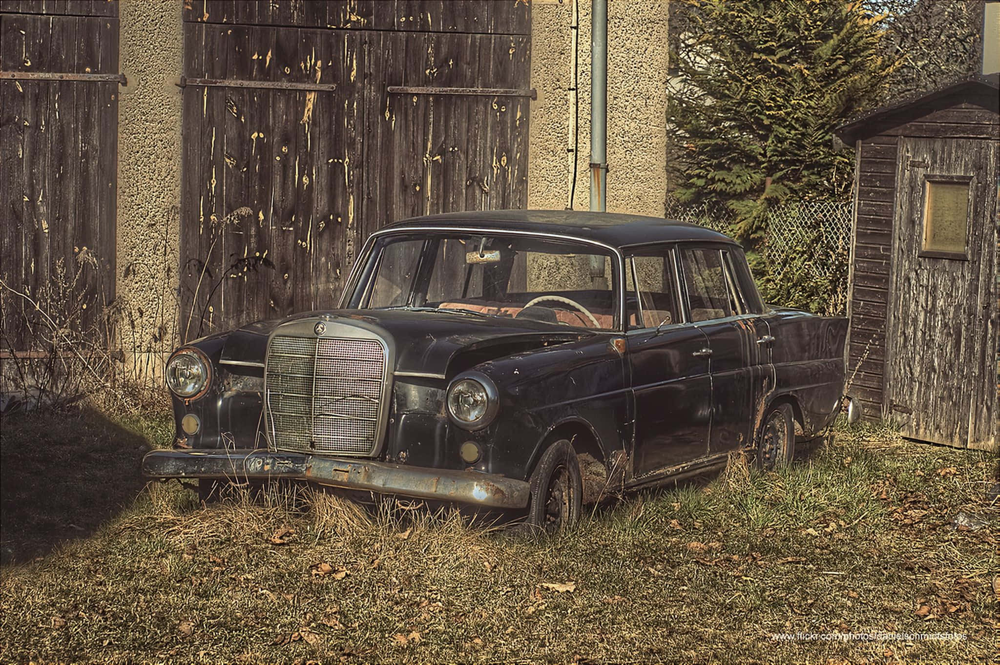Classic Mercedes 桌布 壁紙 — 一輛舊黑色賓士轎車被遺棄在雜草叢生的草地上，旁邊是破舊的木棚和圍欄。