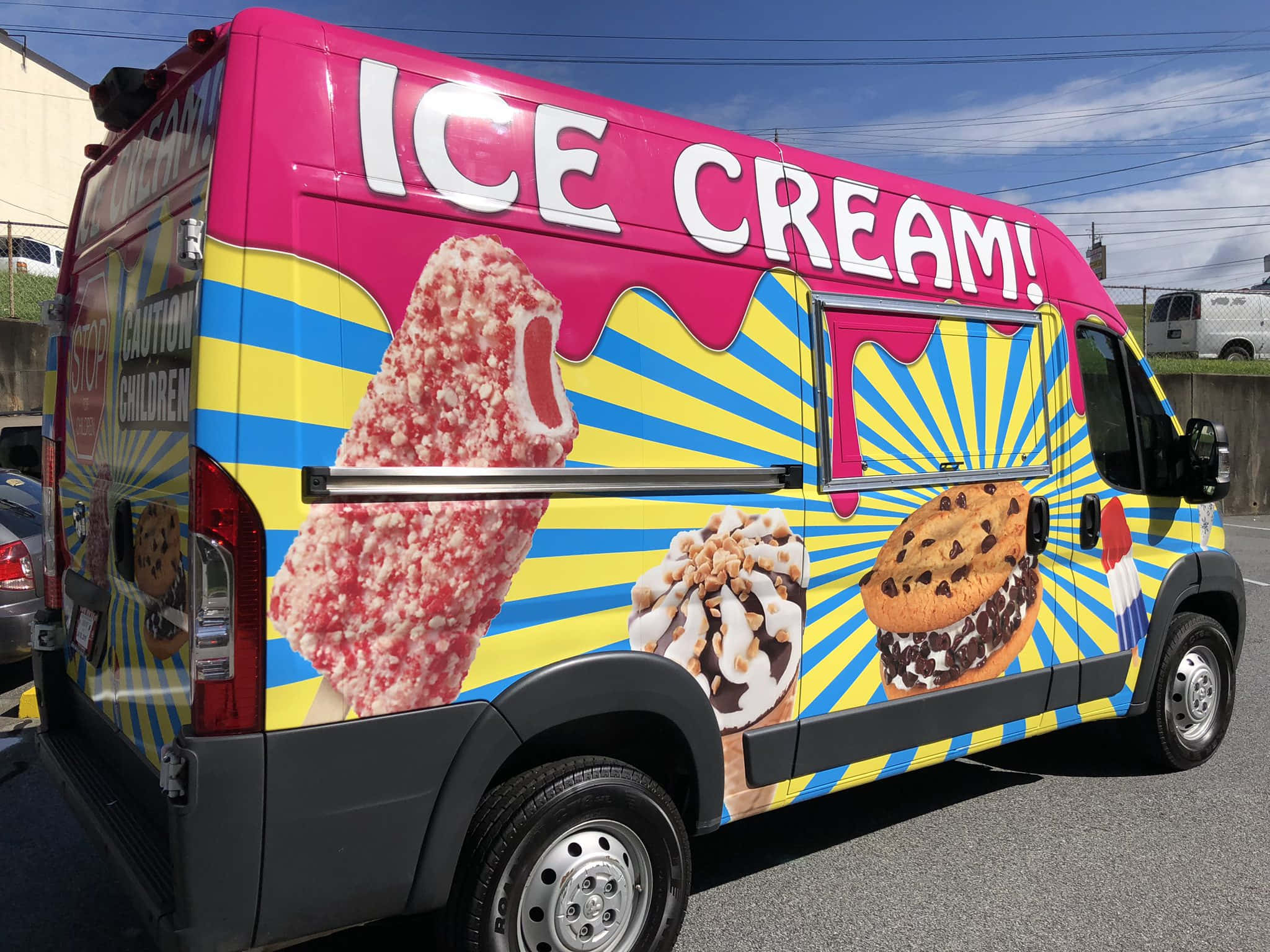 Ice Cream Truck 桌布 壁紙 — 一輛色彩鮮豔的冰淇淋車，帶有醒目的粉紅色、黃色和藍色圖案，在晴朗的藍天下宣傳餅乾三明治和冰棒等美食。