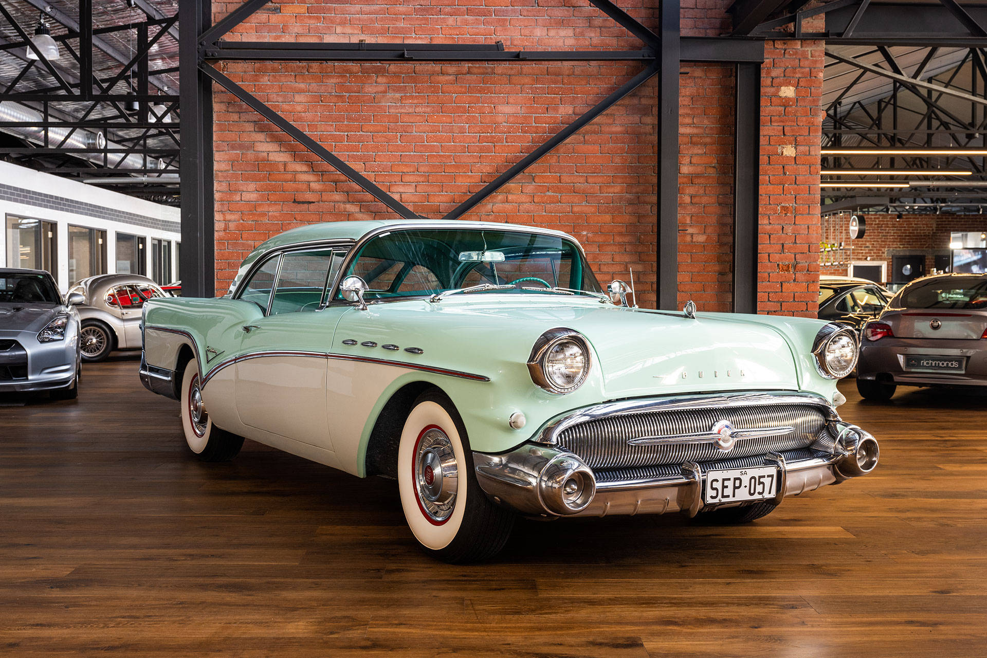 Buick 桌布 壁紙 — 一輛薄荷綠色的1957年Buick Roadmaster配備白色輪胎，在磚牆的經典汽車展廳中，在明亮的燈光下閃閃發光。