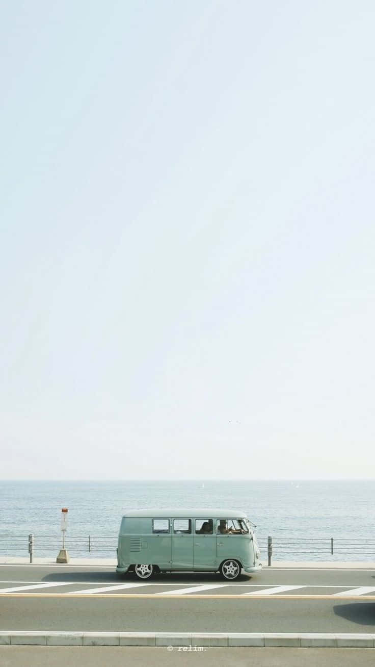 Minimalist Photography 桌布 壁紙 — 一輛薄荷綠色的復古廂型車沿著海岸道路行駛，天空朦朧，平靜的海洋延伸至地平線。