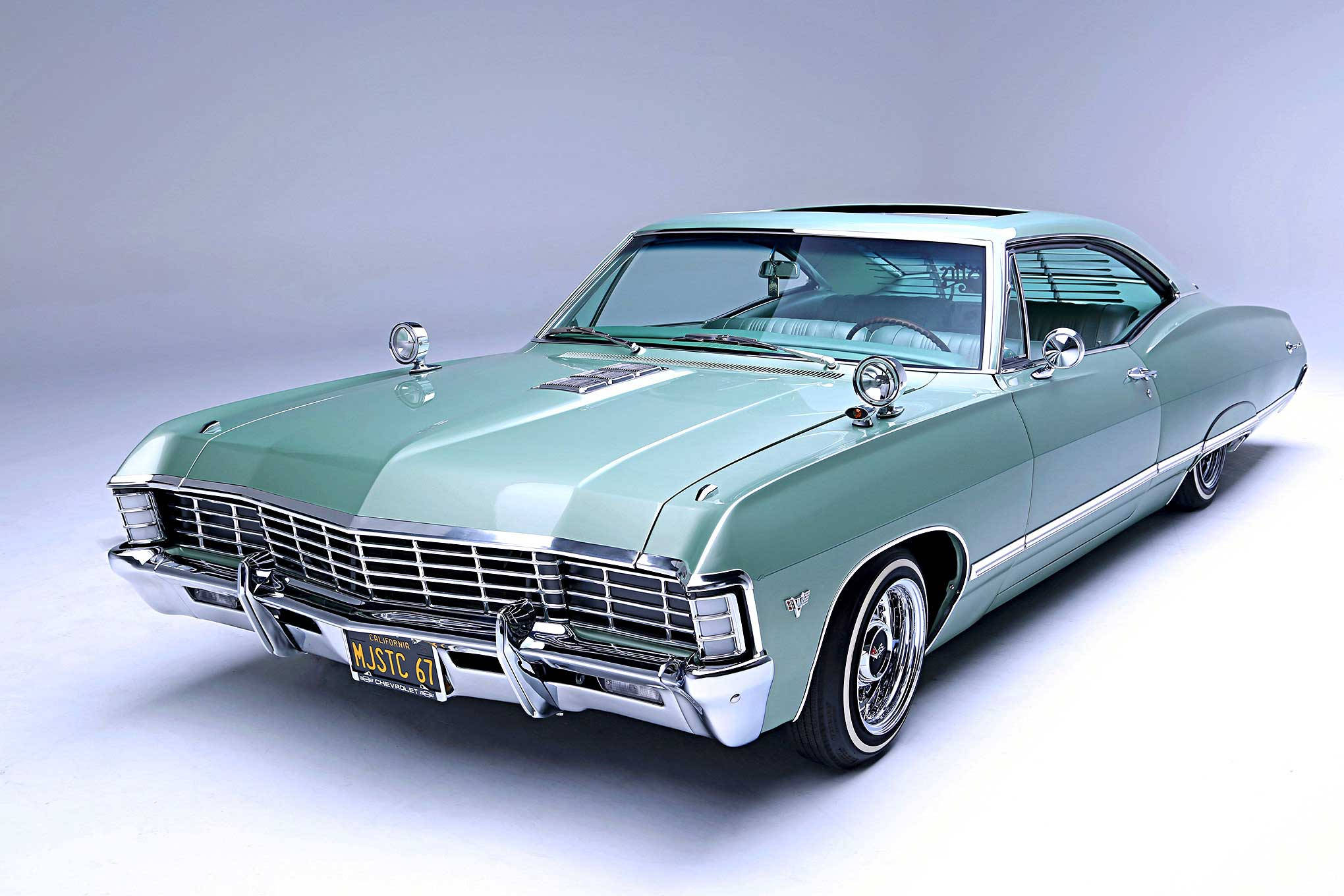 chevrolet impala 1967 桌布 壁紙 — 一輛薄荷綠色的經典美國肌肉車，帶有鍍鉻裝飾和白色輪胎，擺放在灰色工作室背景前。