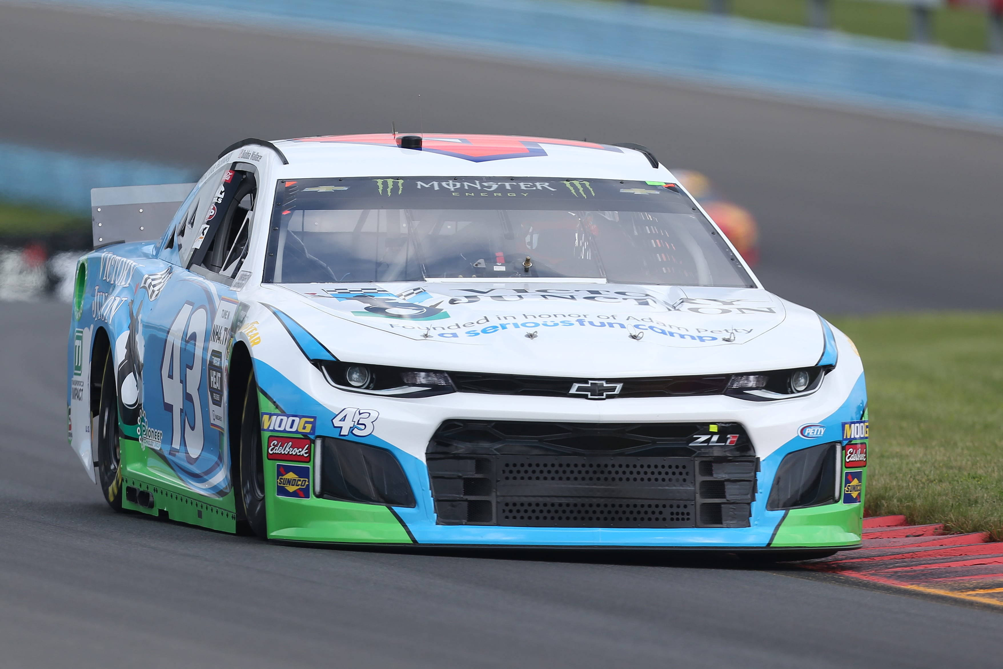 Bubba Wallace 桌布 壁紙 — 一輛藍、綠、白色的NASCAR賽車，編號43，沿著賽道疾馳，經過紅色和黃色的路緣石。