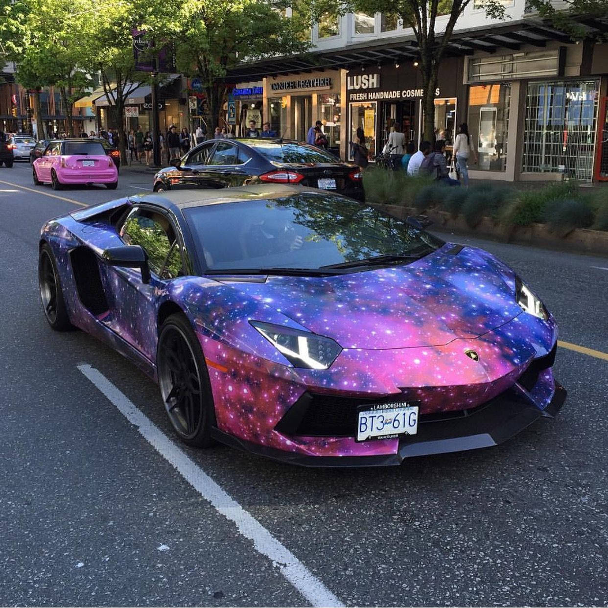 蘭博基尼 桌布 壁紙 — 一輛藍寶堅尼跑車帶有充滿活力的銀河包裝，停在靠近商店的綠樹成蔭的城市街道上。