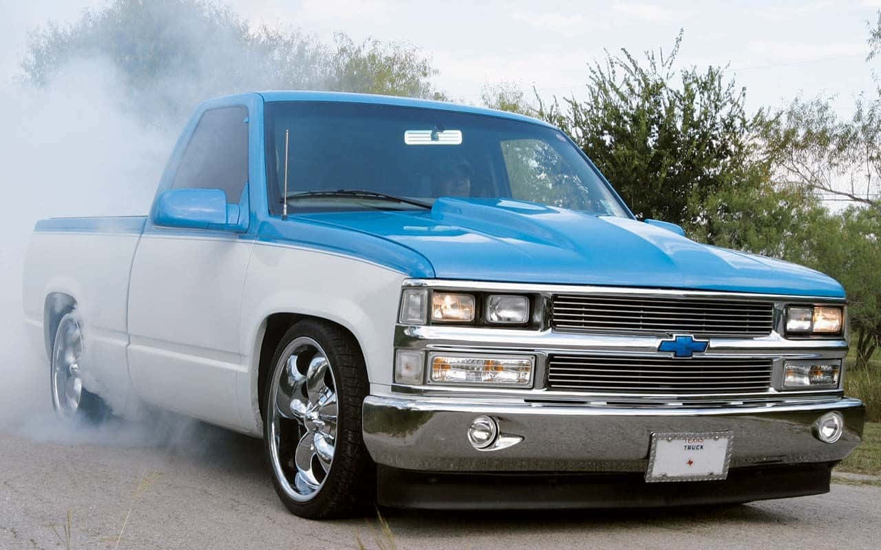 Trucks 桌布 壁紙 — 一輛藍白相間訂製的雪佛蘭皮卡在鋪砌的道路上進行燒胎表演，輪胎冒出滾滾濃煙。