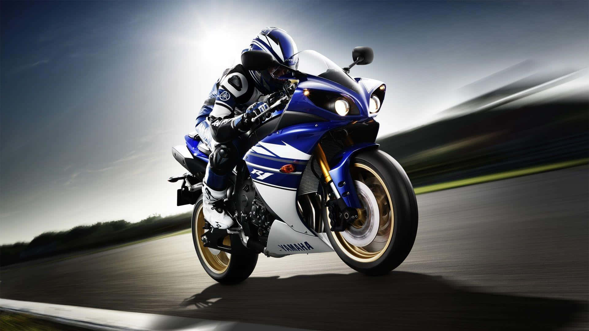 Rider 桌布 壁紙 — 一輛藍白色Yamaha R1摩托車在賽道上高速行駛，帶有動態模糊效果，騎士背後有明亮的陽光。