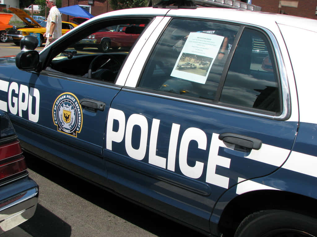 Gotham City Police Department 桌布 壁紙 — 一輛藍白色的GPD警車停放在一個車展上，背景有復古車輛和人群。
