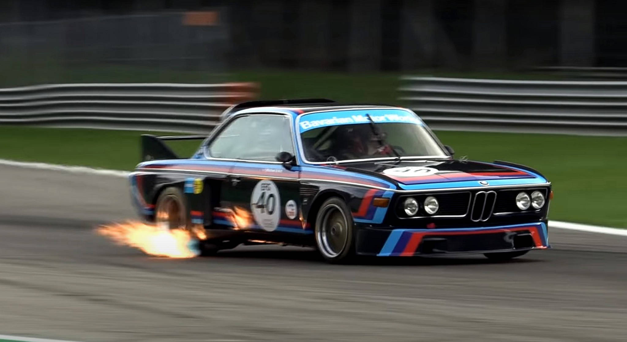 classic bmw 桌布 壁紙 — 一輛藍紅黑配色的復古BMW賽車在賽道上疾馳，輪胎冒煙，背景是模糊的護欄和綠色草地。
