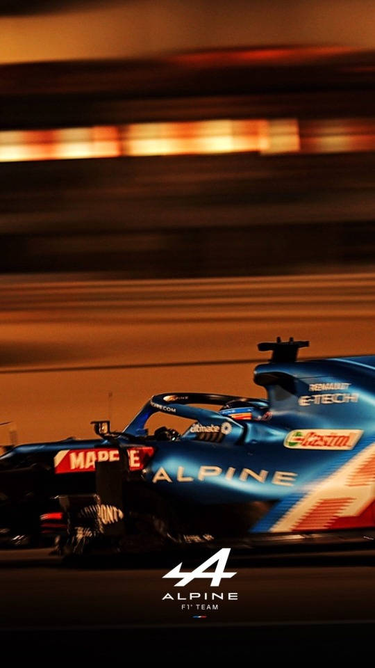 F1 桌布 壁紙 — 一輛藍色 Alpine F1 賽車在夜間高速行駛，身後留下橙色燈光的動態模糊條紋。