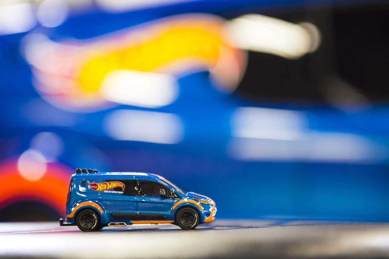 Hot Wheels 桌布 壁紙 — 一輛藍色 Hot Wheels 玩具貨車帶有橙色點綴，在模糊多彩的散景背景前清晰對焦。