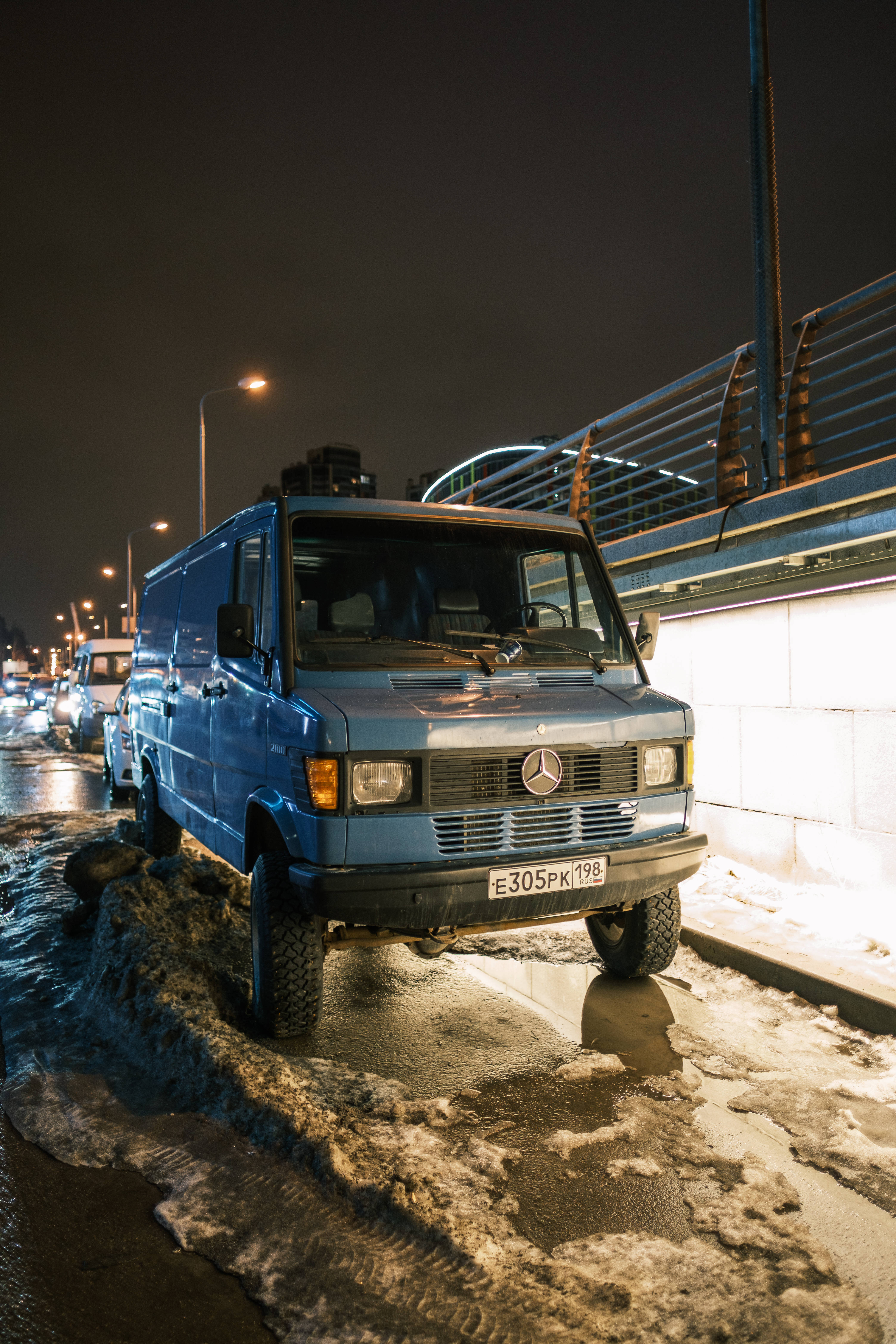 Mercedes Amg 桌布 壁紙 — 一輛藍色 Mercedes-Benz 客貨車在夜間停泊在積雪的市區街道上，街燈在濕雪上投射出倒影。