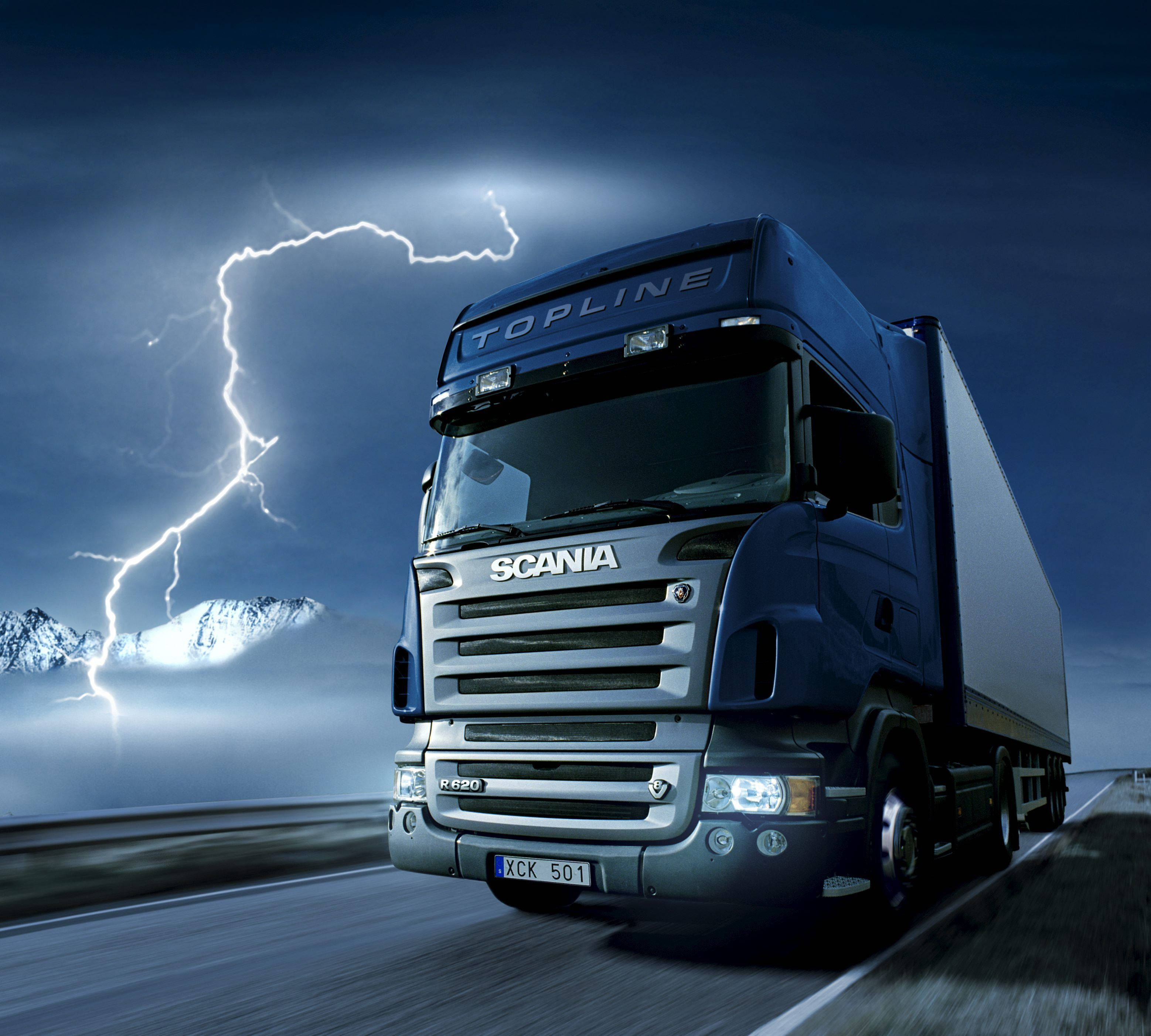 American Truck Simulator 桌布 壁紙 — 一輛藍色 Scania Topline 卡車在高速公路上疾駛，閃電擊中暴風雨天空下積雪覆蓋的山脈。