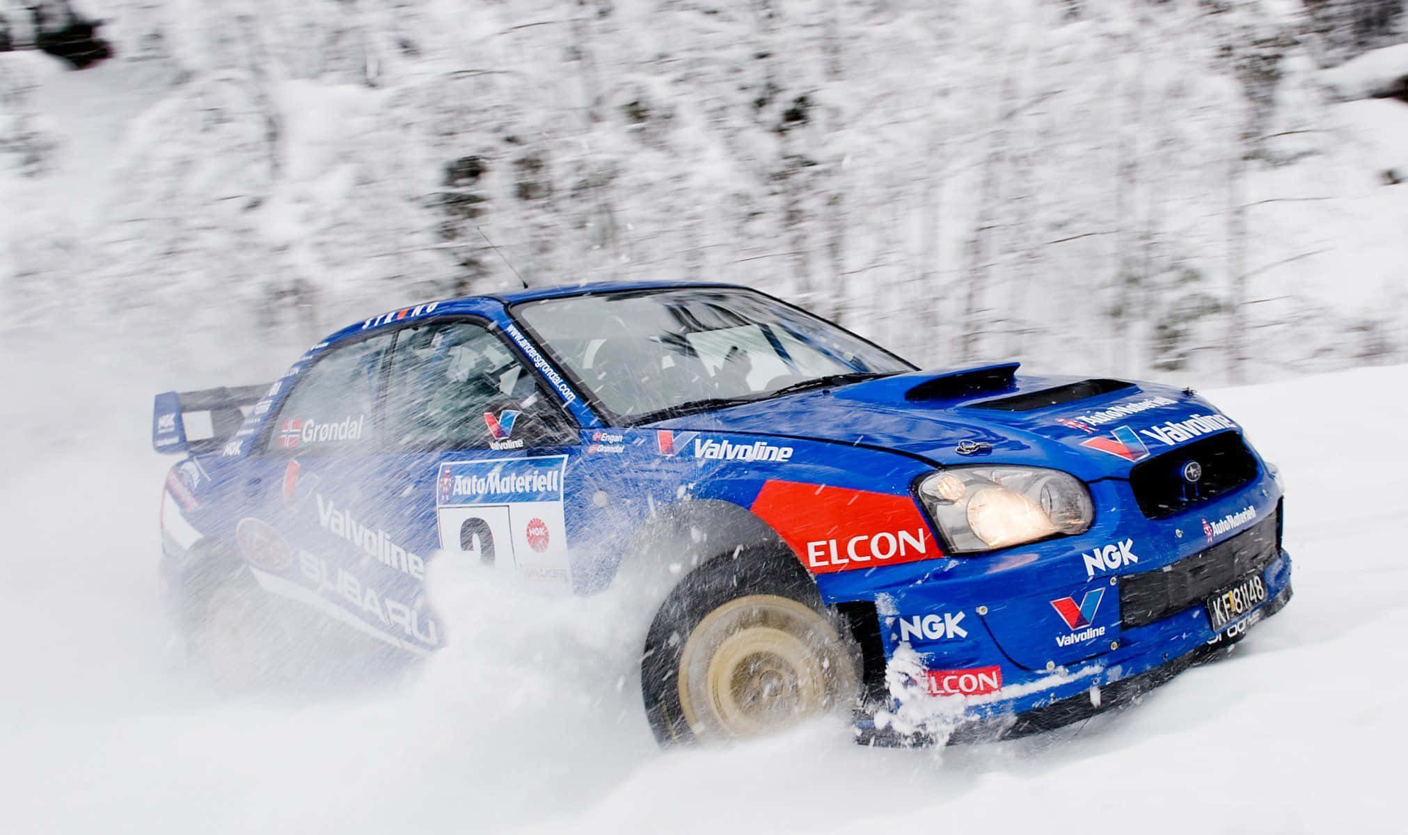 Ice Racing 桌布 壁紙 — 一輛藍色 Subaru 拉力賽車在白雪覆蓋的森林小徑上疾馳，揚起白色粉末。
