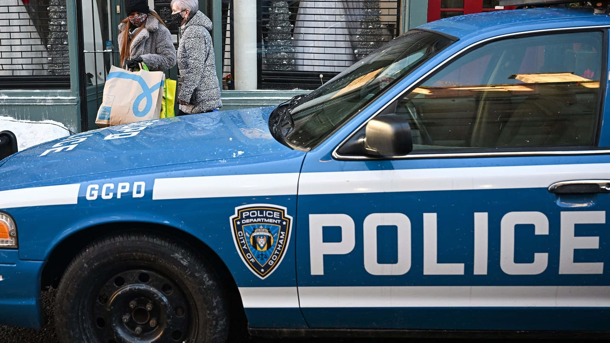 Gotham City Police Department 桌布 壁紙 — 一輛藍色GCPD警車停在積雪的街道上，兩名行人提著購物袋走過。