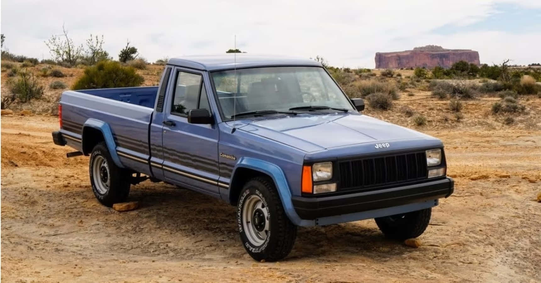 Jeep Comanche 桌布 壁紙 — 一輛藍色Jeep Cherokee皮卡車停在塵土飛揚的沙漠小徑上，背景是紅色岩層。