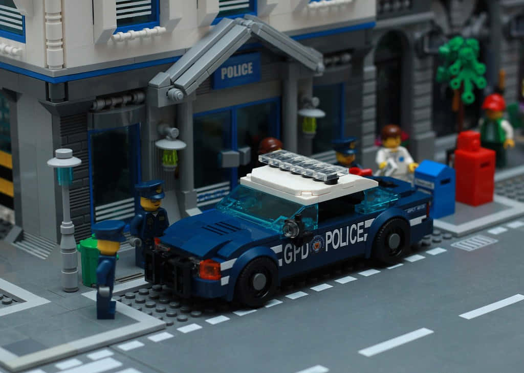Gotham City Police Department 桌布 壁紙 — 一輛藍色LEGO警車停放在LEGO警察局外，配有迷你人偶和街道細節。