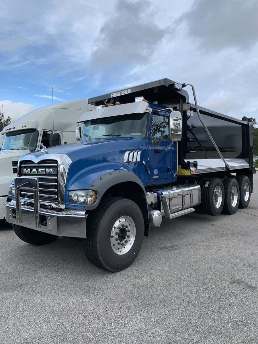 Dump Truck 桌布 壁紙 — 一輛藍色Mack自卸卡車帶有鍍鉻裝飾，停在瀝青路面上，天空多雲，後面可見一輛白色半掛卡車。