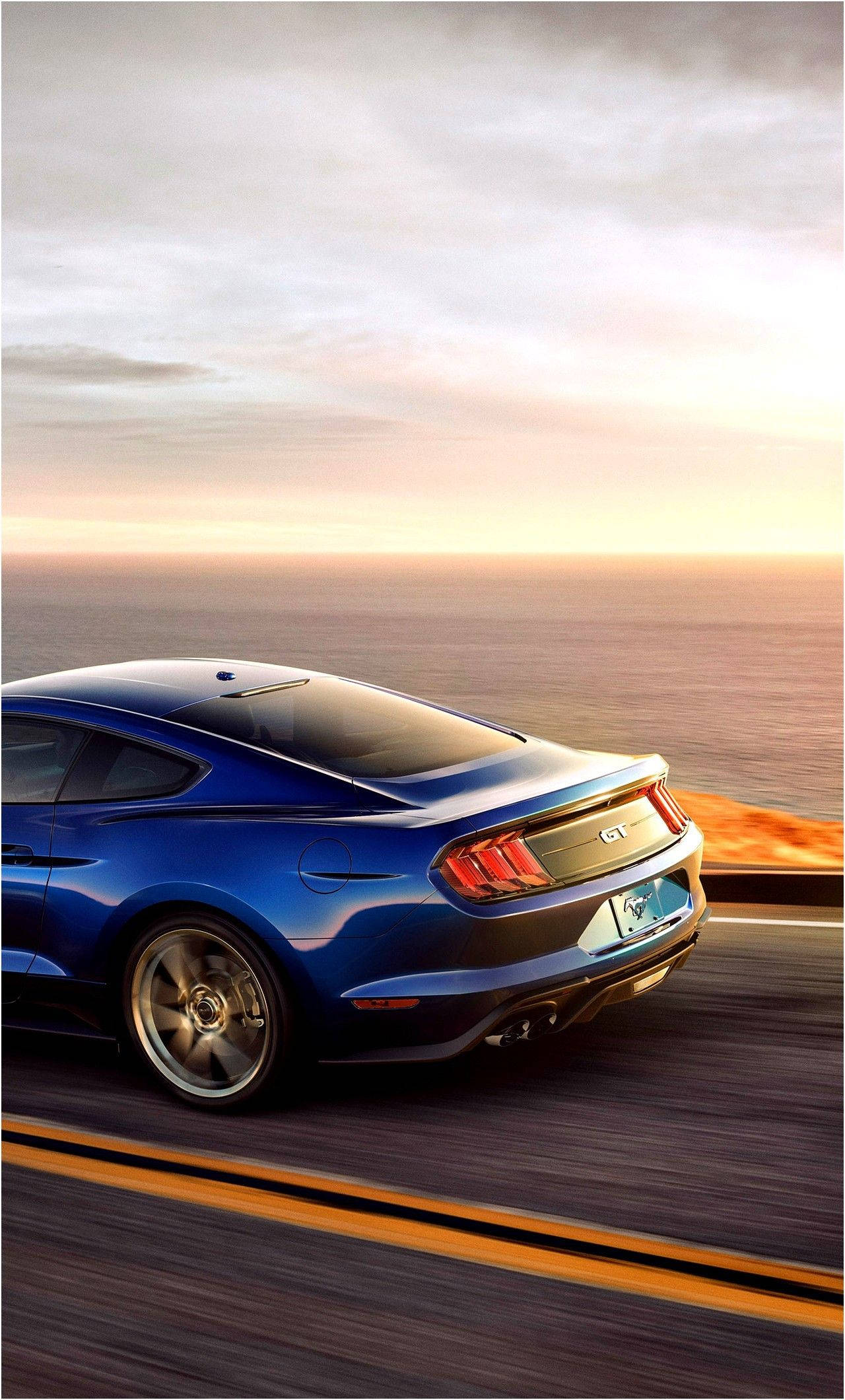 ford iPhone 桌布 壁紙 — 一輛藍色Mustang GT在日落時分沿著海岸高速公路疾馳，帶有模糊的動態和溫暖的金色天空。
