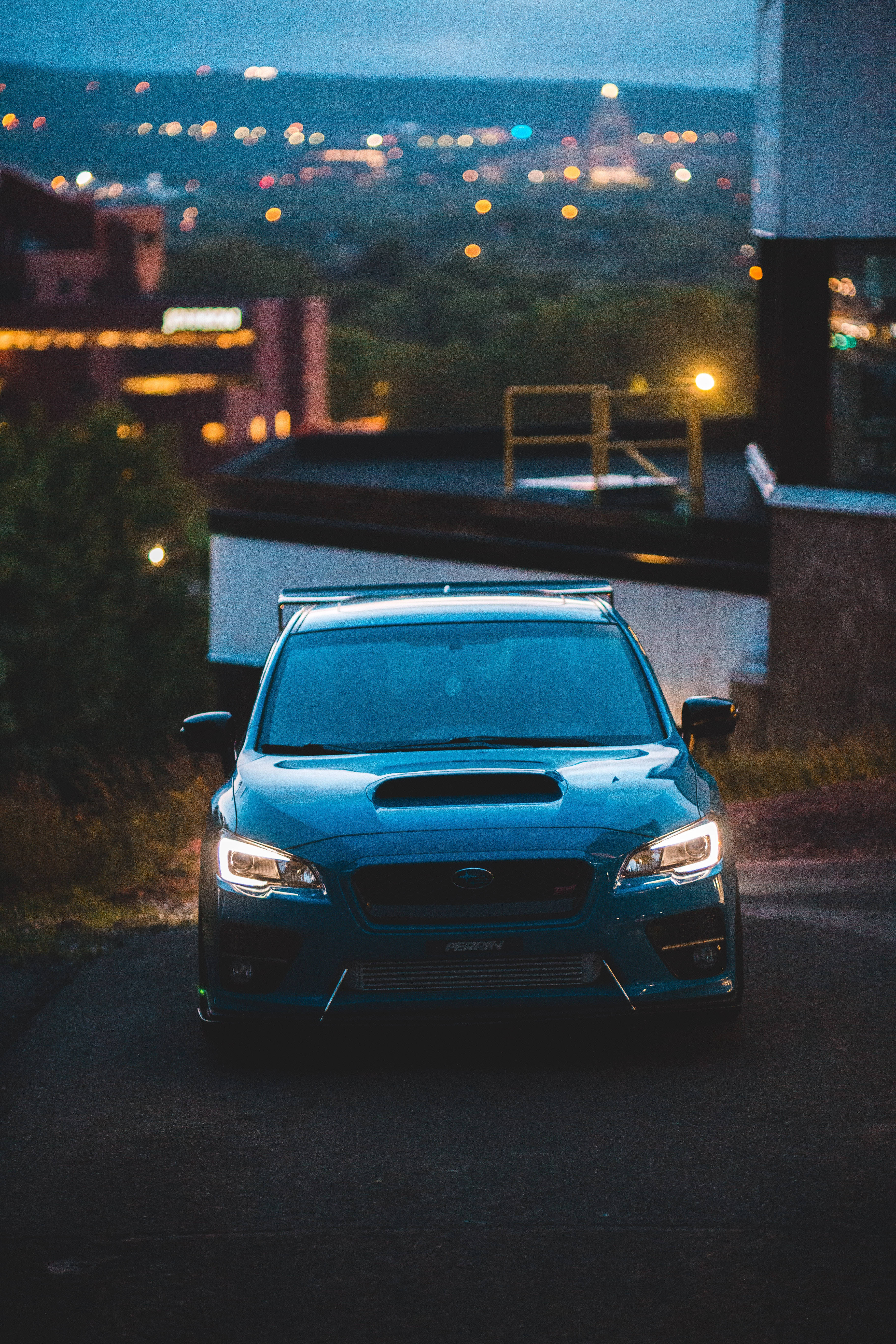 昴 桌布 壁紙 — 一輛藍色Subaru WRX STI在黃昏時停泊在屋頂上，背景中城市燈光閃爍。